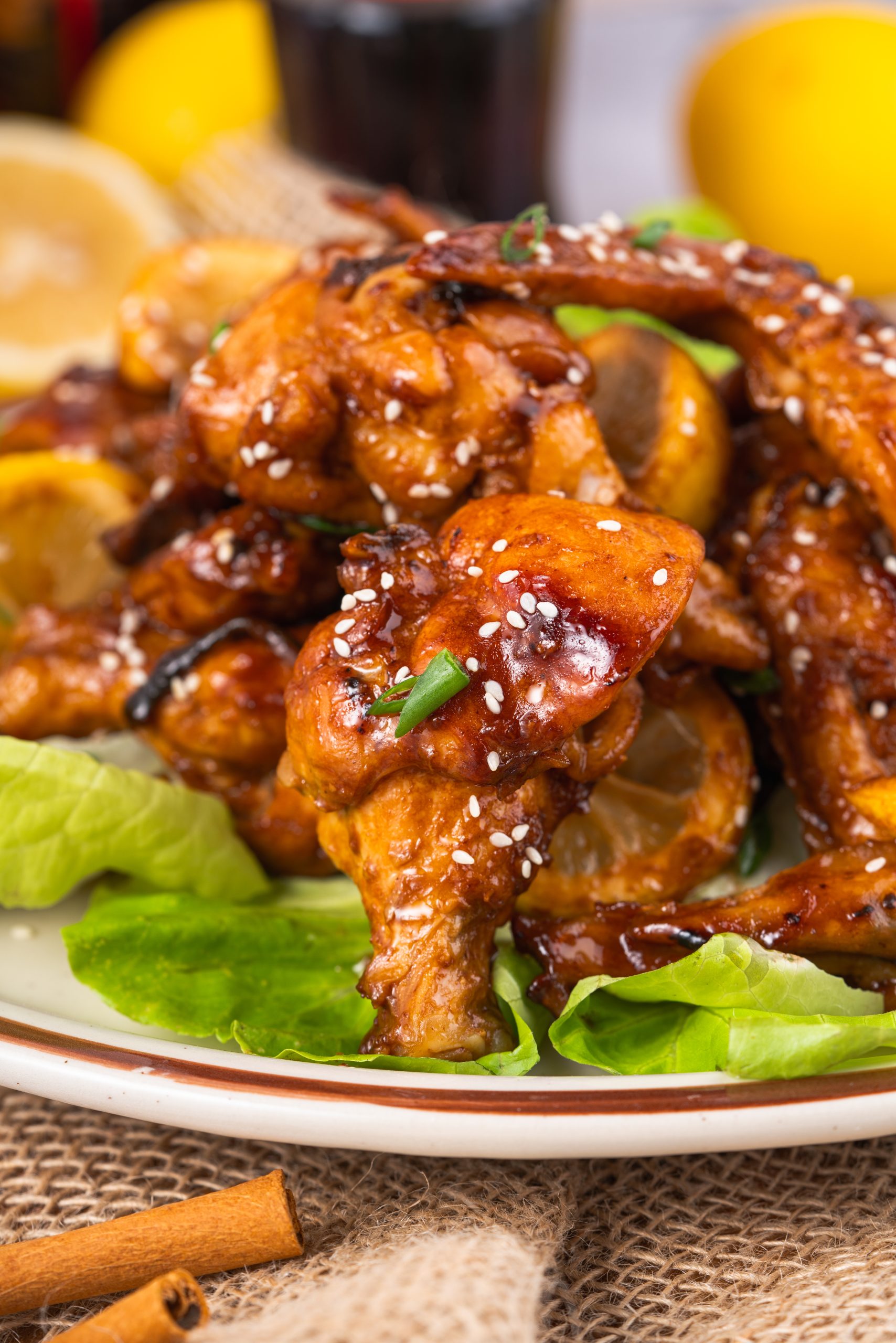Close-up of Coca Cola Chicken Wings stacked on lettuce leaves, showcasing the sticky glaze and charred lemon slices.