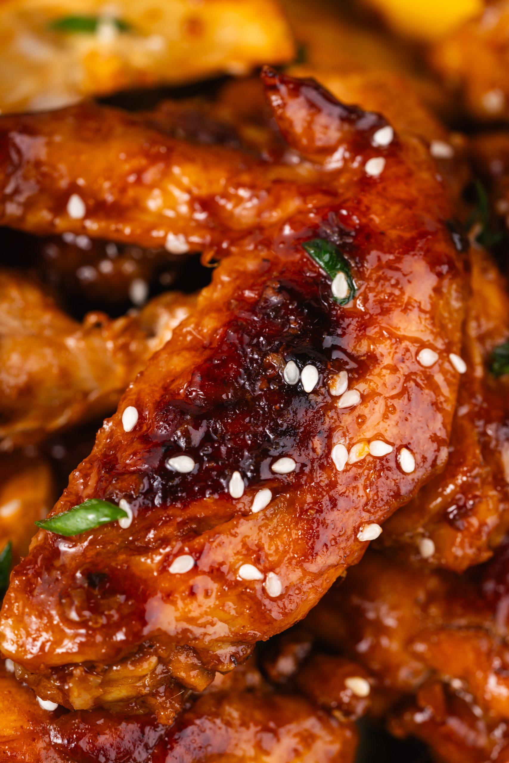 Macro shot of a single Coca Cola Chicken Wing with golden glaze and visible white sesame seeds, sitting on crisp lettuce.