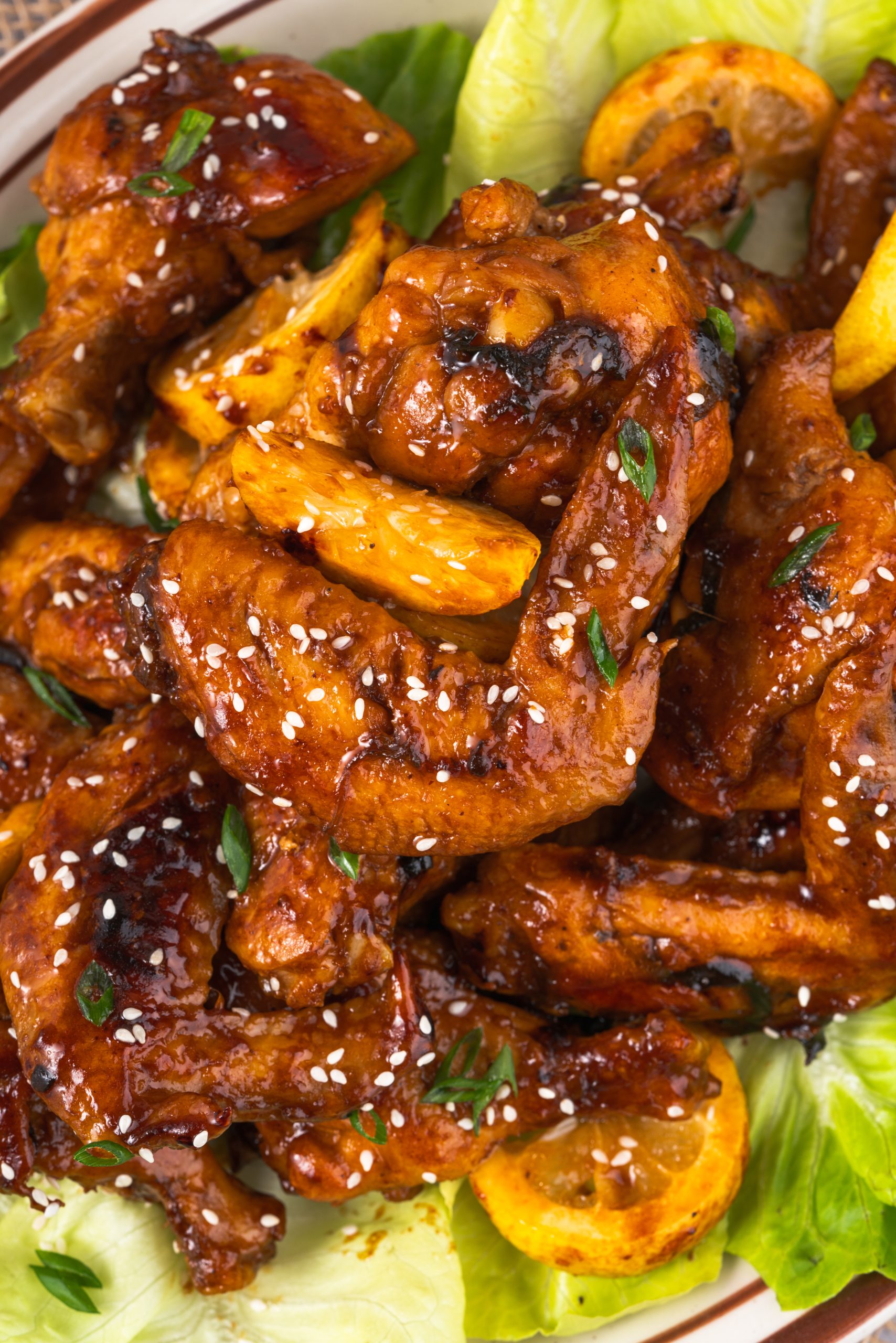 Top-down close-up of Coca Cola Chicken Wings showing texture of glaze, golden lemon slices, and vibrant green garnish.