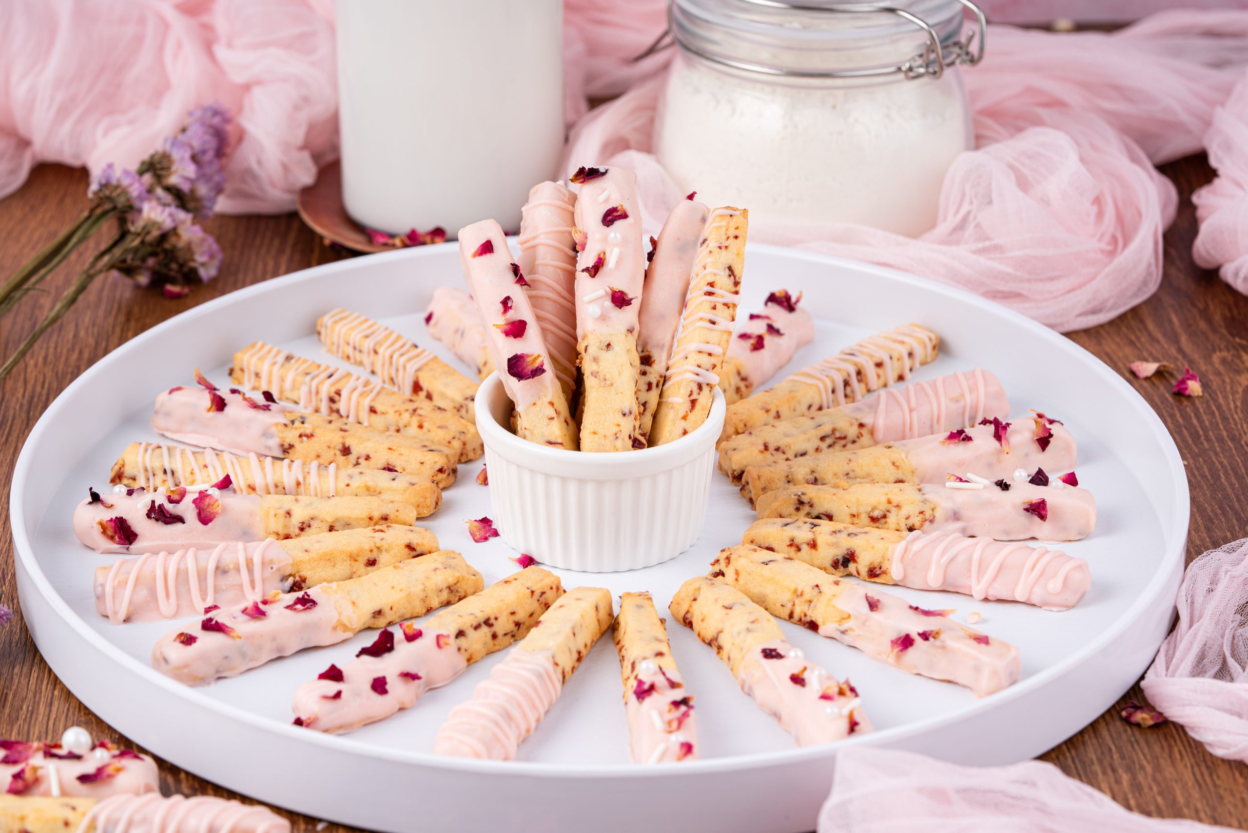 Cranberry Cookies decorated with pink chocolate drizzle and rose petals, arranged in a circular display on a white platter.