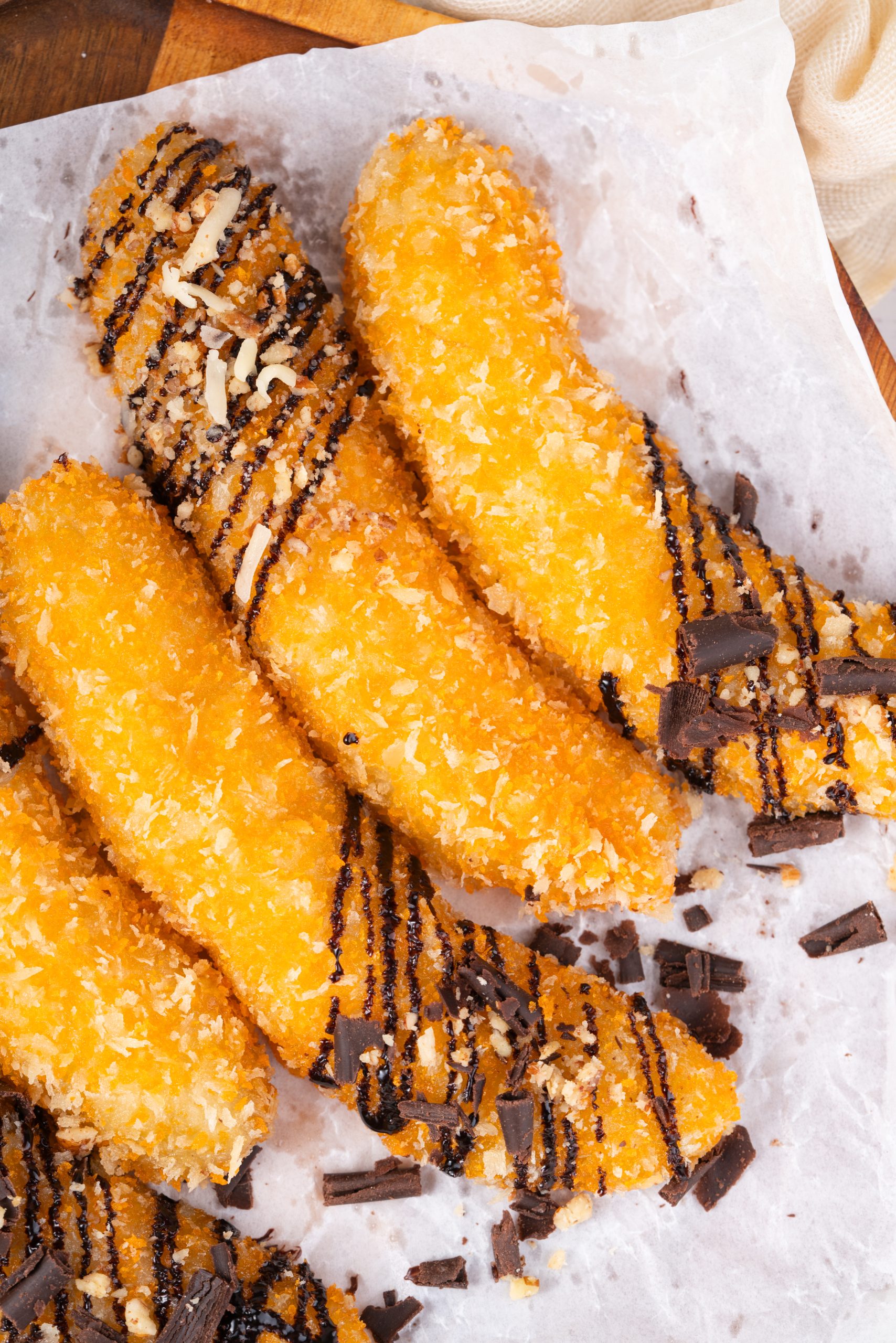 Close-up of crunchy banana fritters with chocolate drizzle on parchment paper