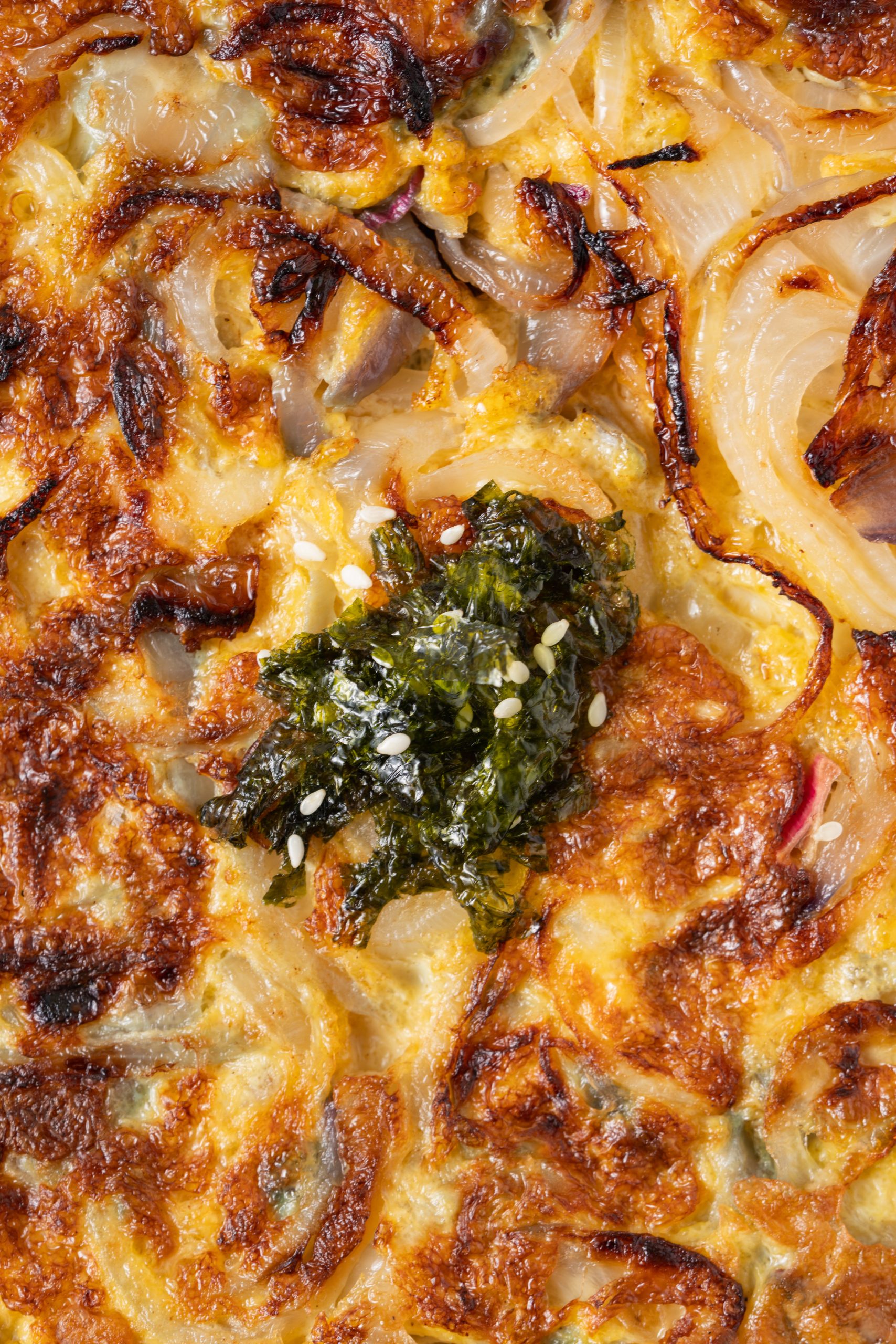 Close-up of a Chinese onion omelette recipe showing caramelized onions, fluffy eggs, and a topping of seaweed and sesame seeds.