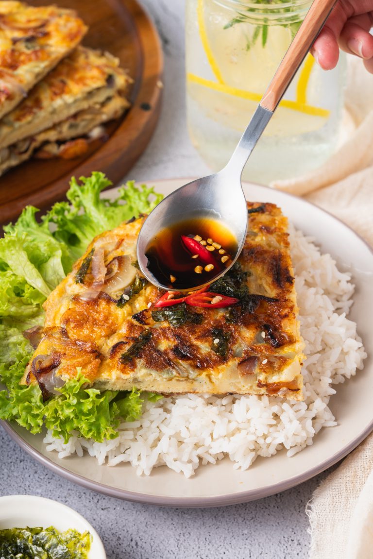 Savory Chinese onion omelette recipe served on a bed of white rice with lettuce and topped with soy sauce and red chili slices.