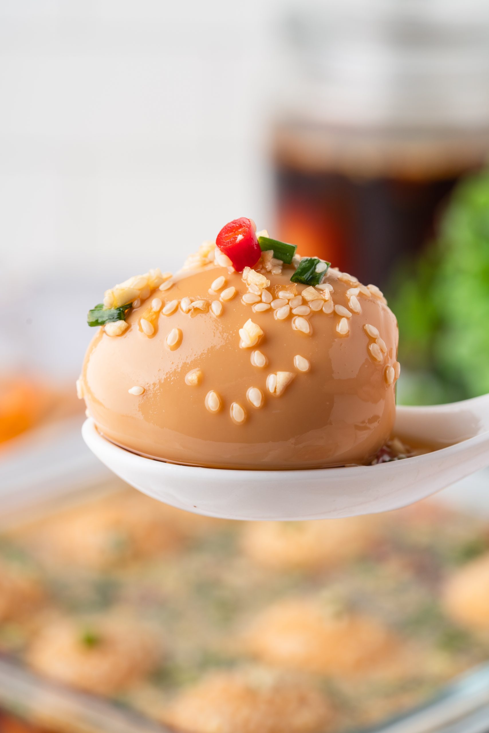 Korean Marinated Egg topped with sesame seeds, garlic, scallions, and red chili on a white spoon