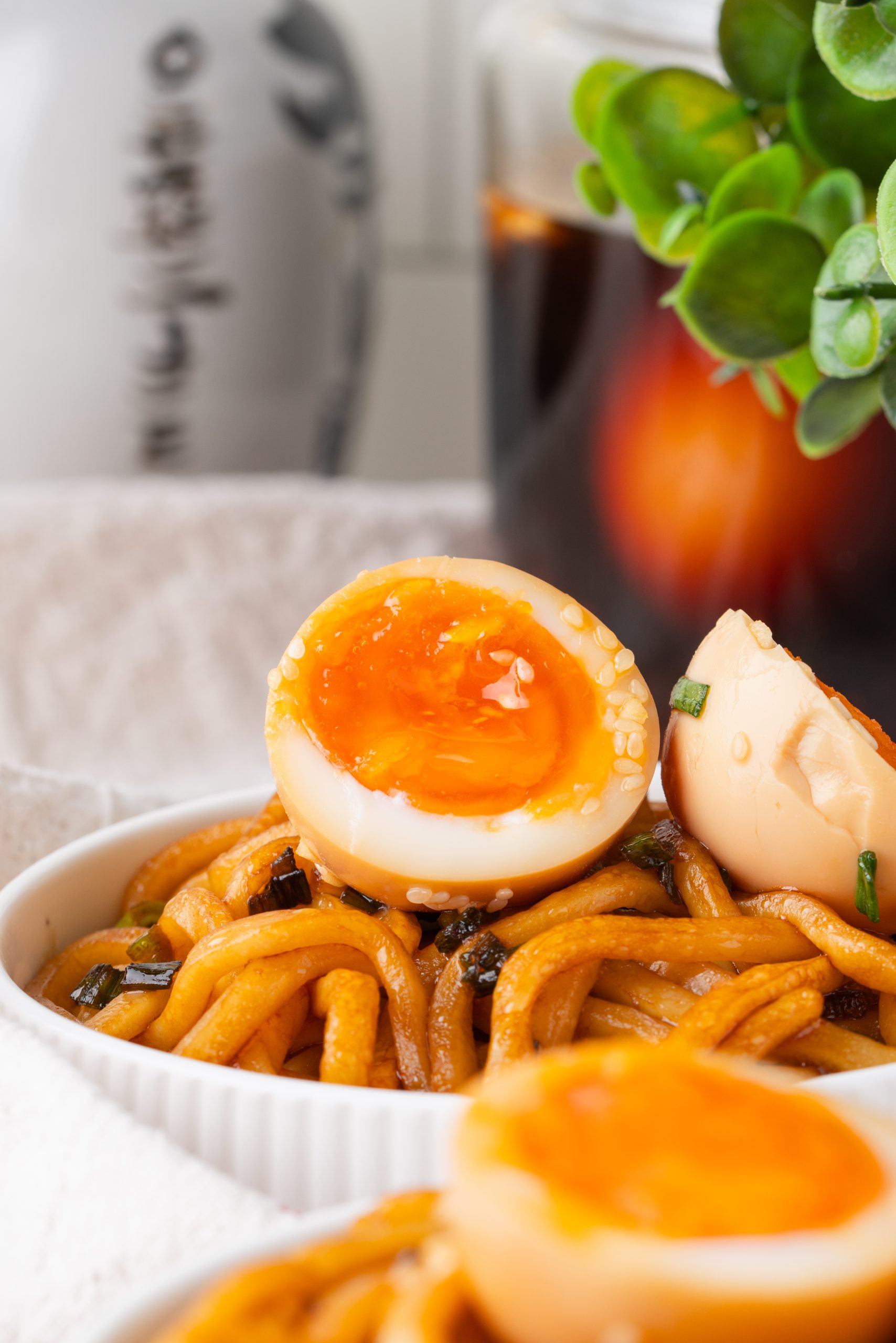 Close-up of jammy Korean Marinated Egg on top of savory stir-fried udon noodles with scallions