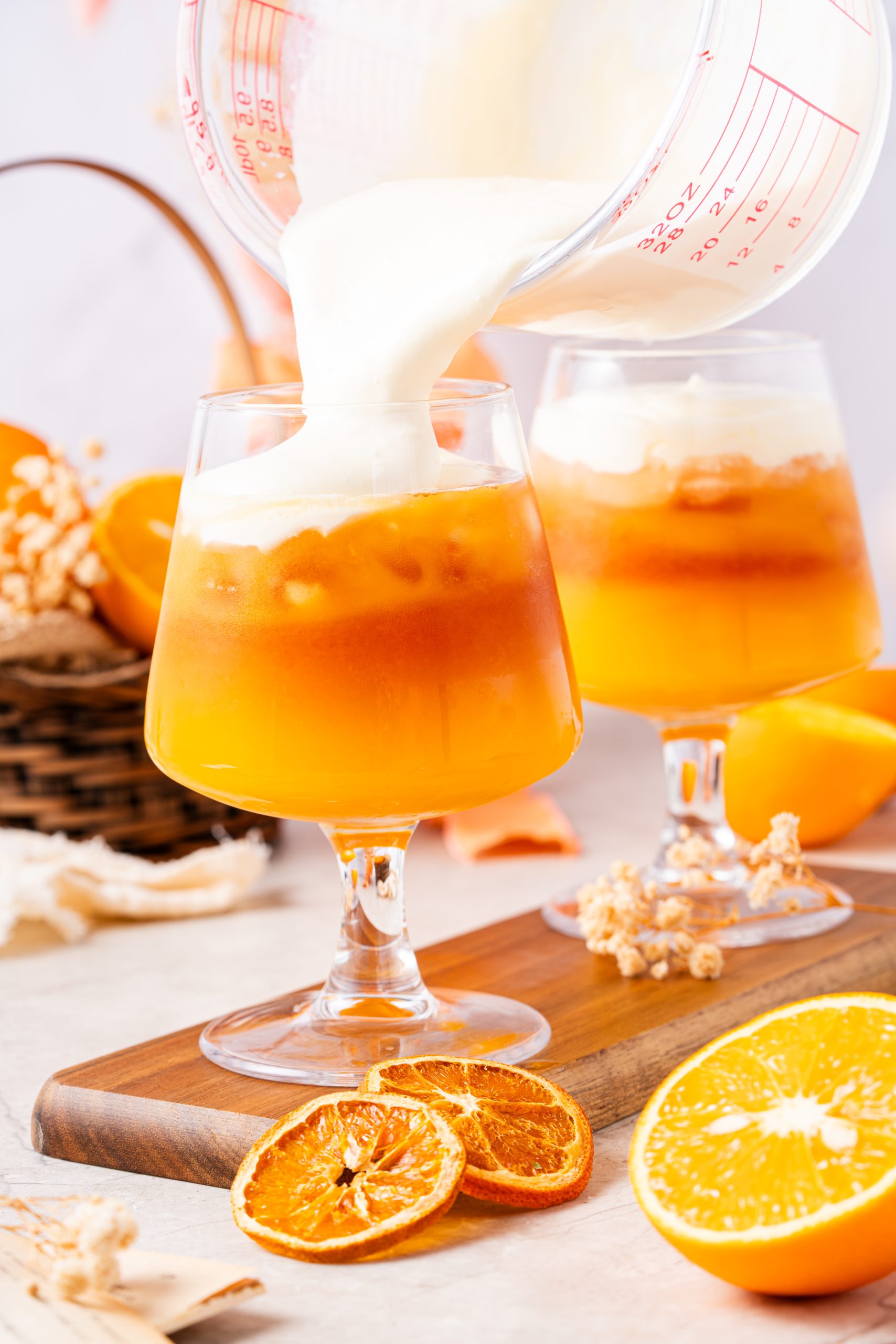 Creamy cheese foam being poured over iced orange Earl Grey tea in a clear glass, showcasing a vibrant layered drink with a rich, velvety top.