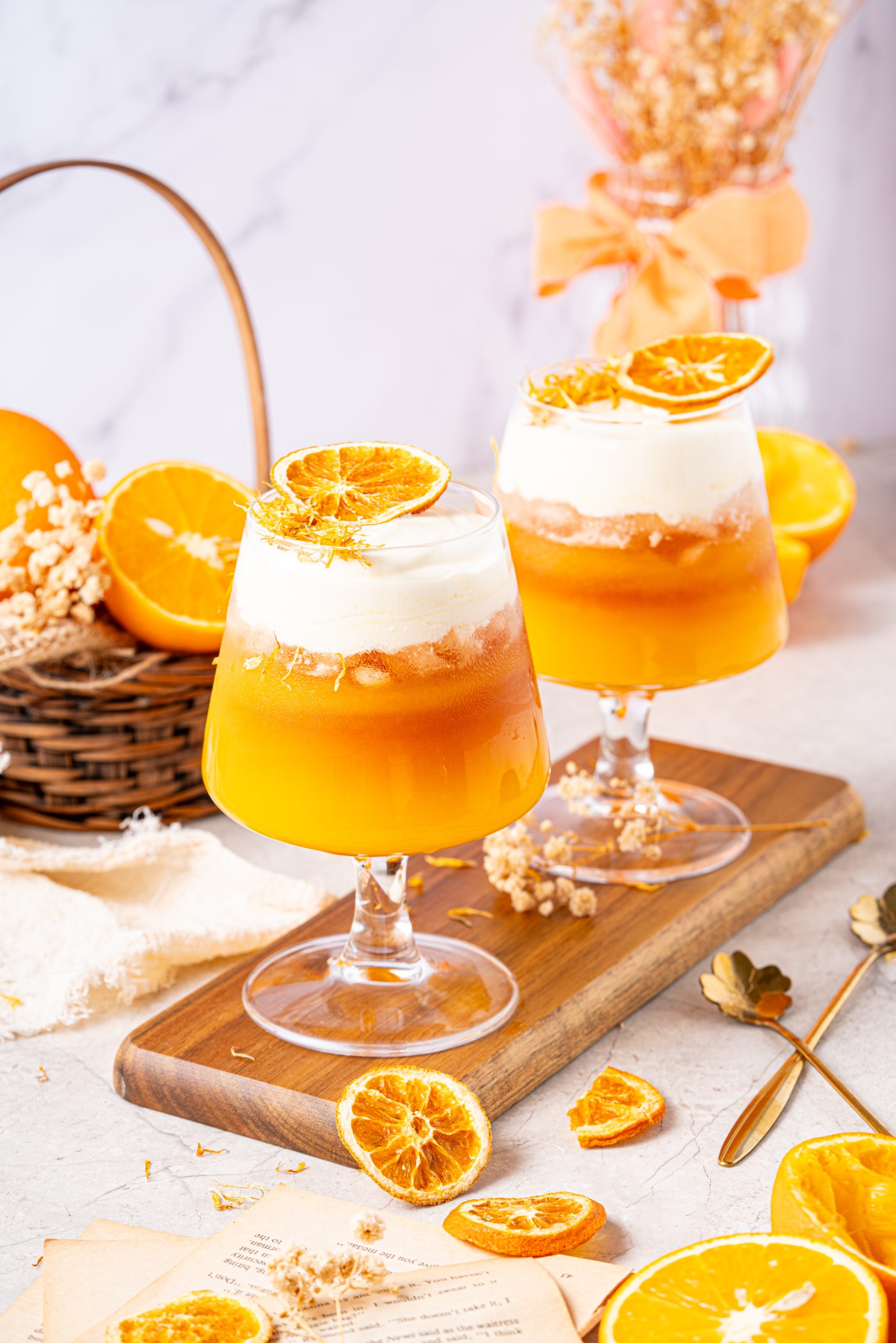 Front view of citrusy orange tea with layered cheese foam and dried orange garnish, elegantly presented on a wooden board with rustic orange and floral decor.