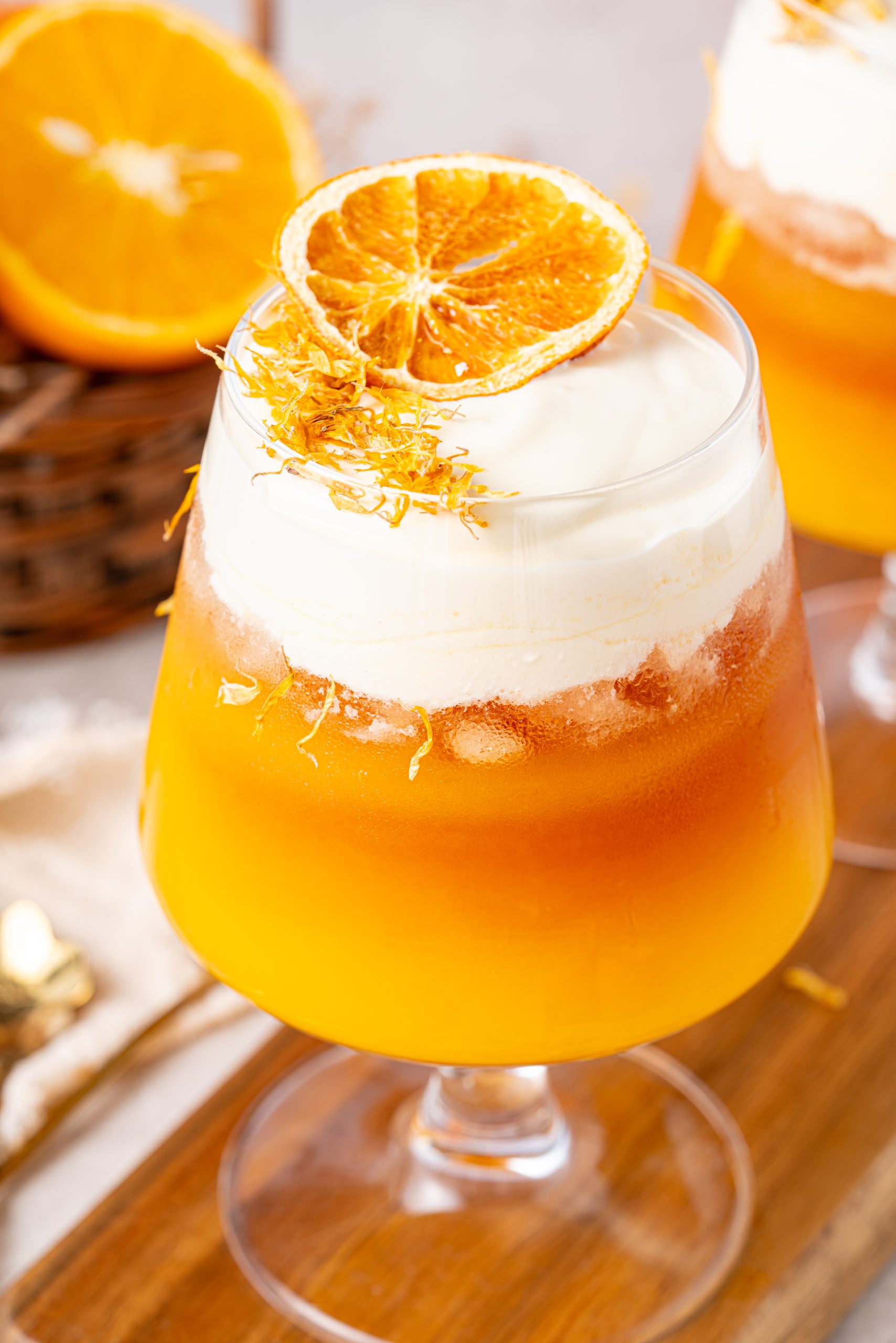 Close-up of a vibrant orange tea layered with creamy cheese foam, topped with a dried orange slice and delicate floral shreds.