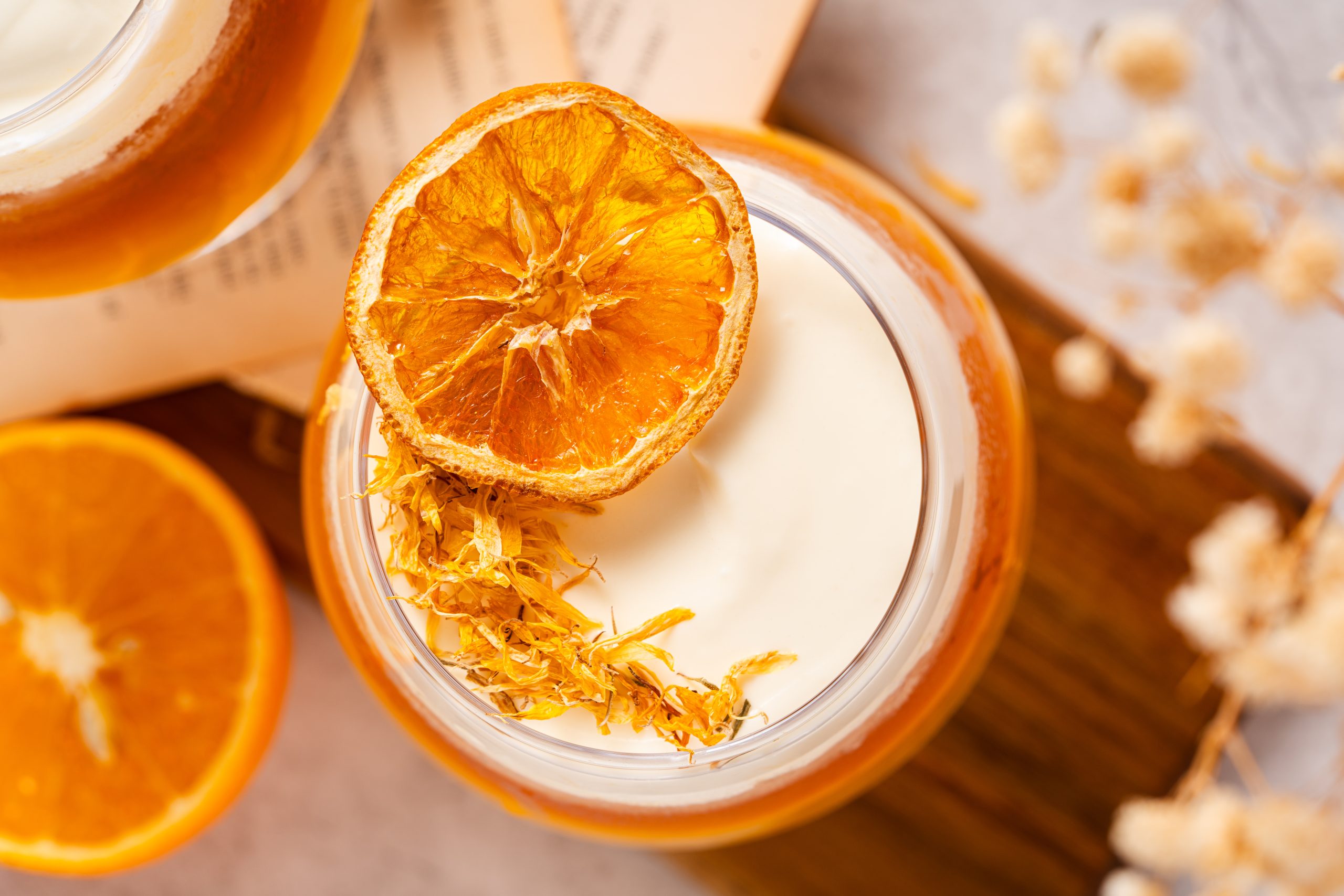 Top view of an orange tea with cheese foam, garnished with a dried orange slice and edible yellow flower petals, styled on a wooden board with soft floral accents.