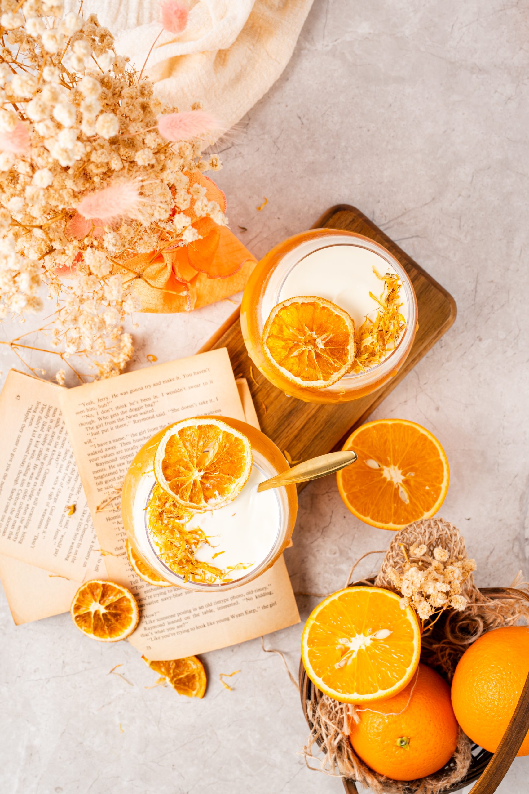 Overhead view of beautifully styled orange Earl Grey tea drinks with cheese foam and dried citrus garnish, surrounded by books, oranges, and dried blooms.