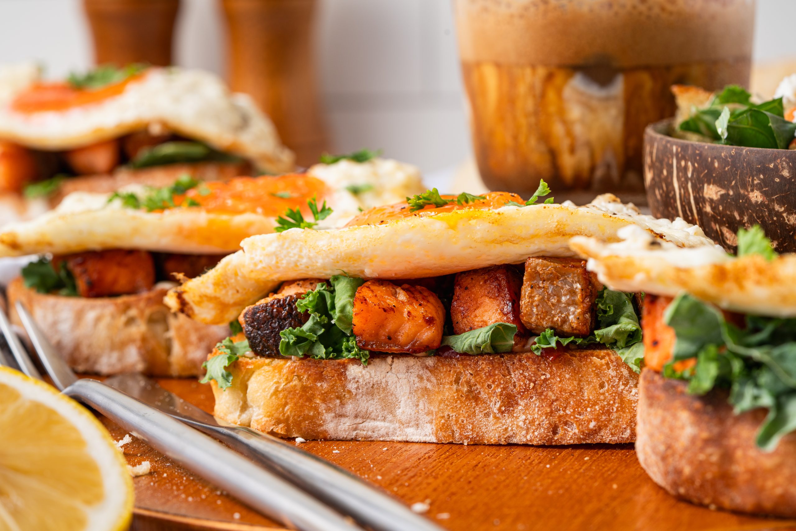 Side view of hearty Salmon Sandwiches layered with greens, seared salmon, and fried eggs on artisan sourdough, perfect for brunch or breakfast.