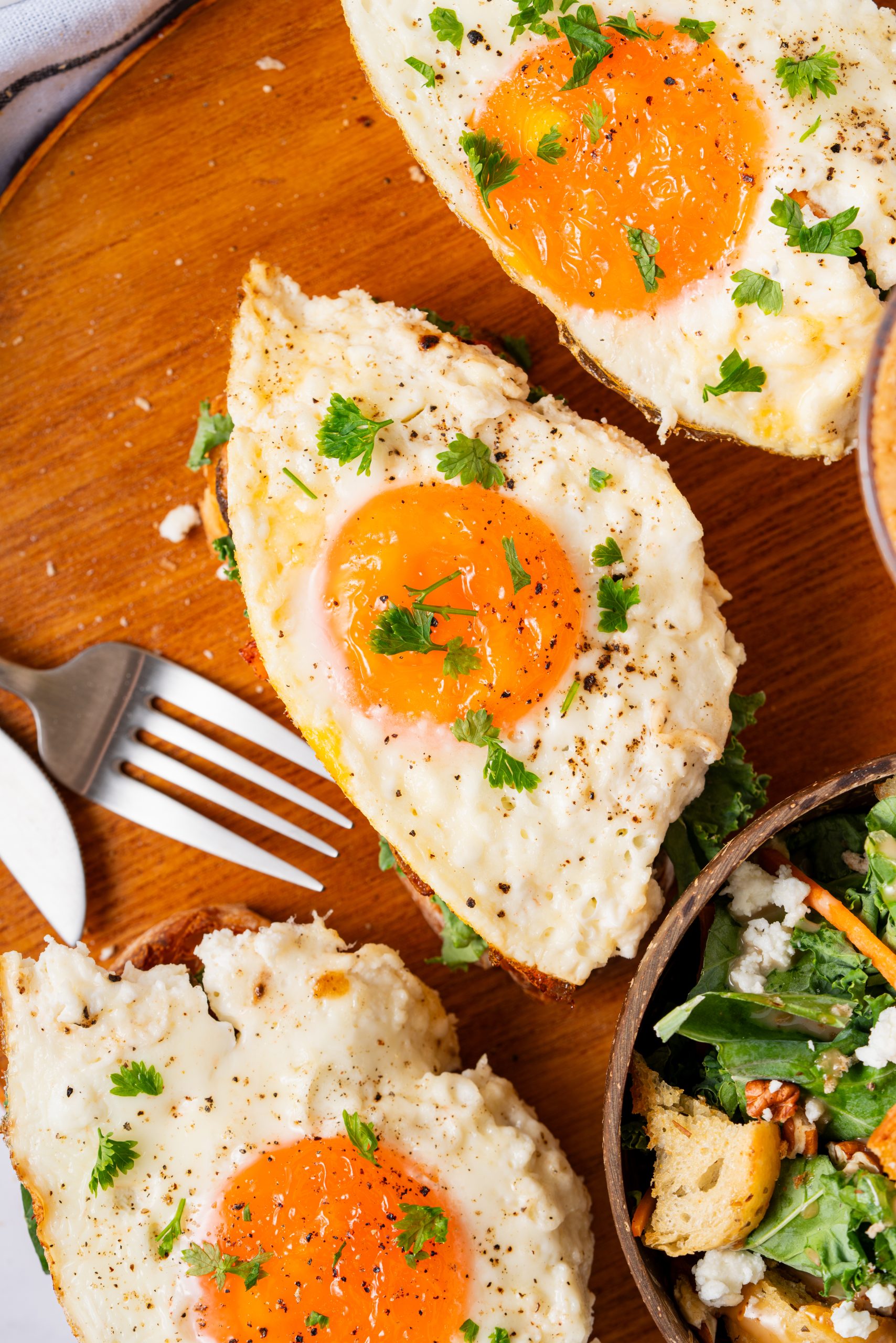 Top view of Salmon Sandwiches with fried eggs, feta, and greens, arranged on a wooden serving board with salad and coffee.