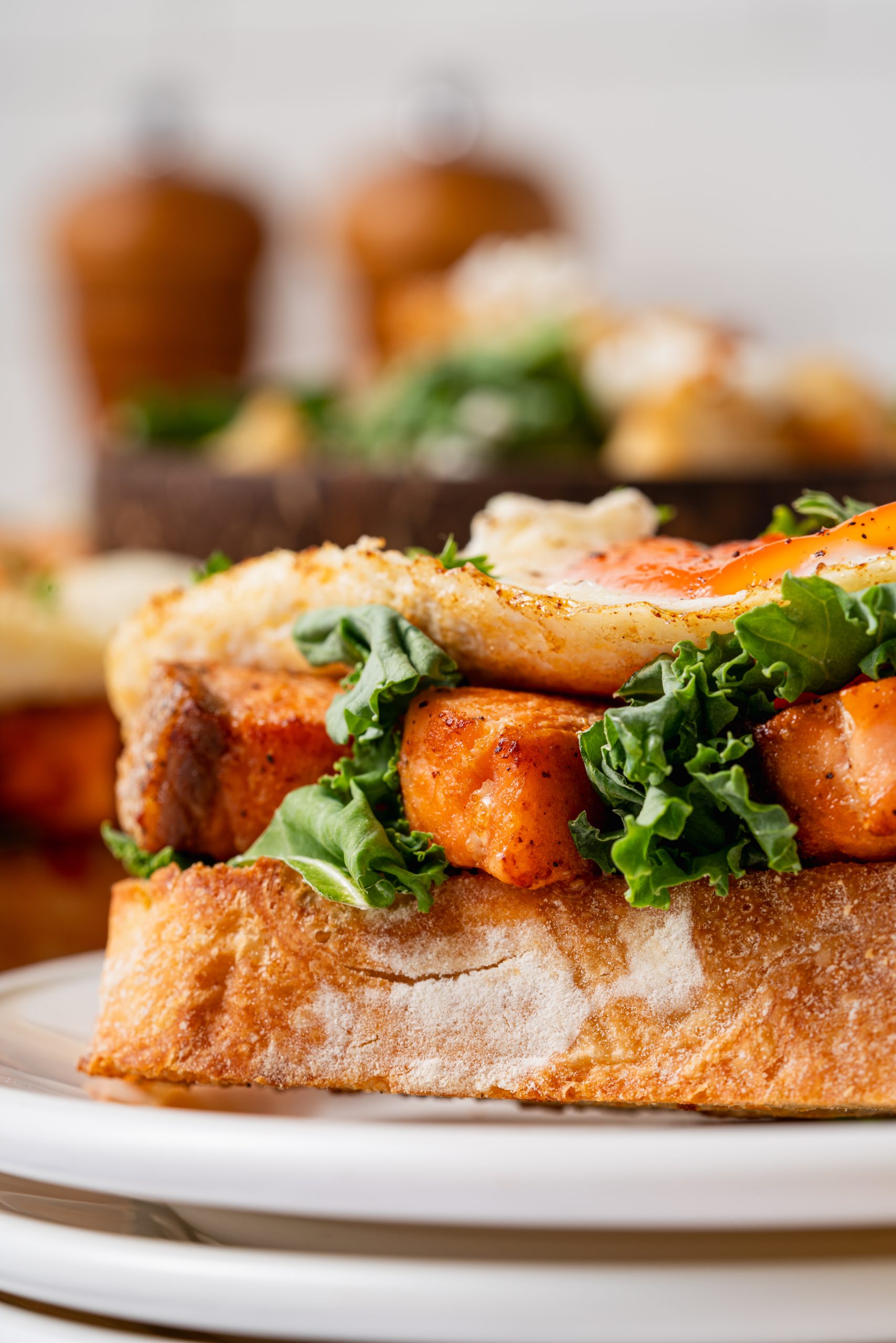 Close-up shot of open-faced Salmon Sandwiches with crispy bread, kale, and soft fried eggs, emphasizing the texture and freshness.