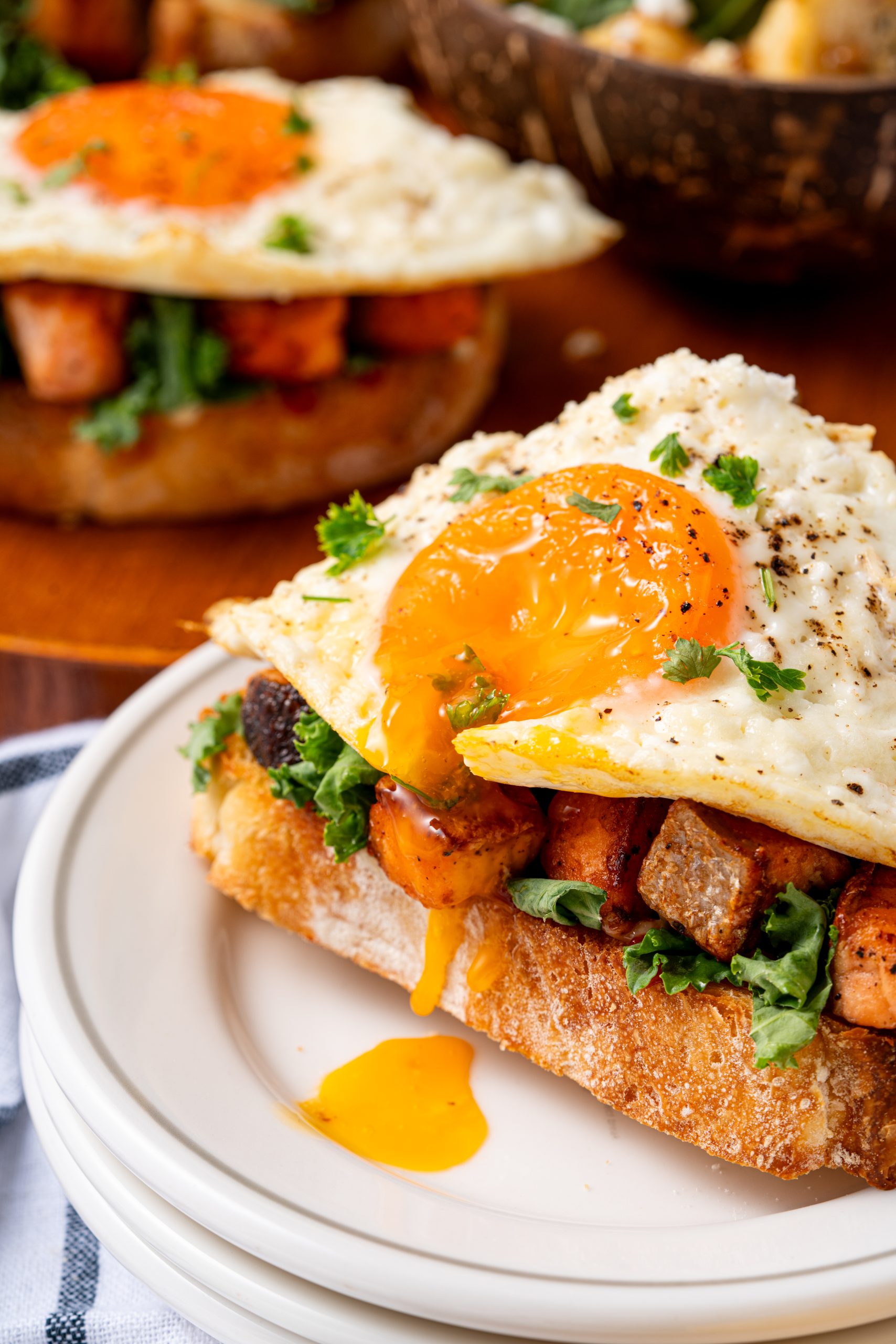 Delicious Salmon Sandwich with runny egg yolk dripping over grilled salmon and leafy greens on toasted bread, served on a white plate.