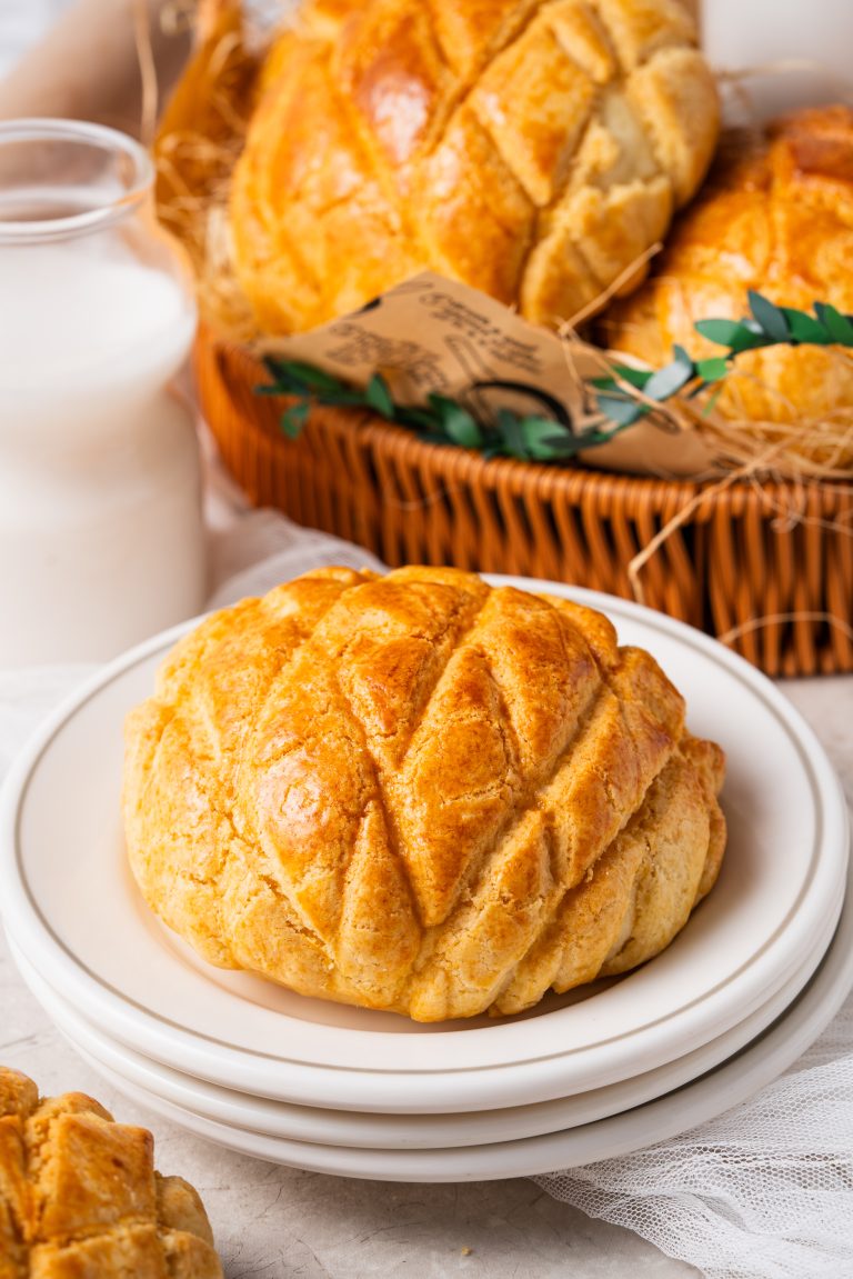A soft and fluffy Pineapple Bun served on a white plate beside a basket of buns and a bottle of milk.