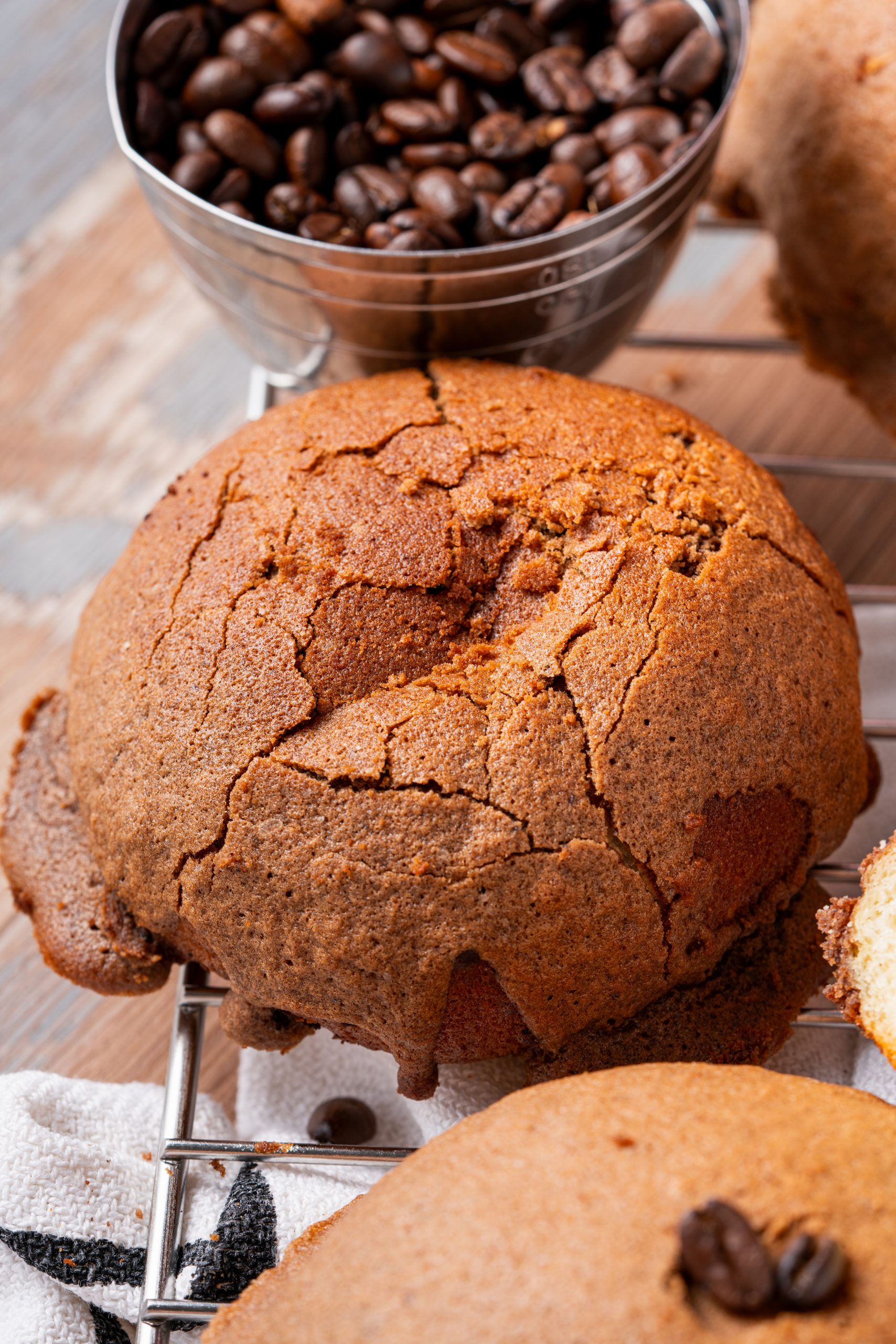Close-up of a round Pappa Roti bun showing its crispy coffee crust beside a cup filled with coffee beans.