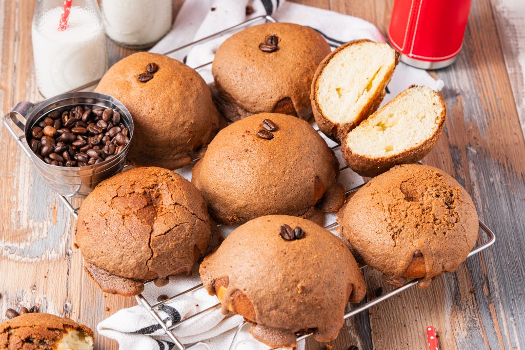 A batch of Pappa Roti buns displayed with coffee beans, milk bottles, and a red coffee tumbler on a rustic table.