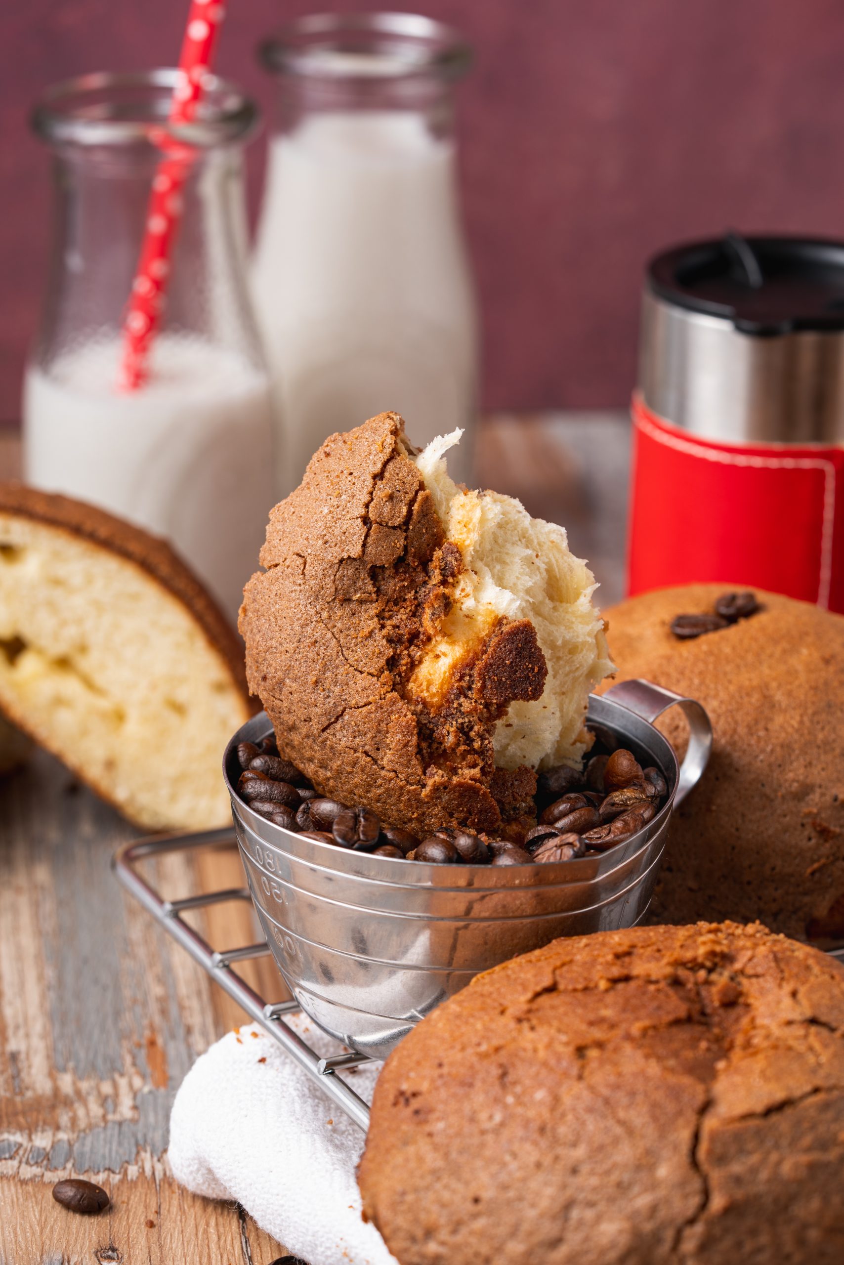 Freshly baked Pappa Roti coffee bun with a cracked golden crust served with milk and coffee beans on a rustic wooden table.