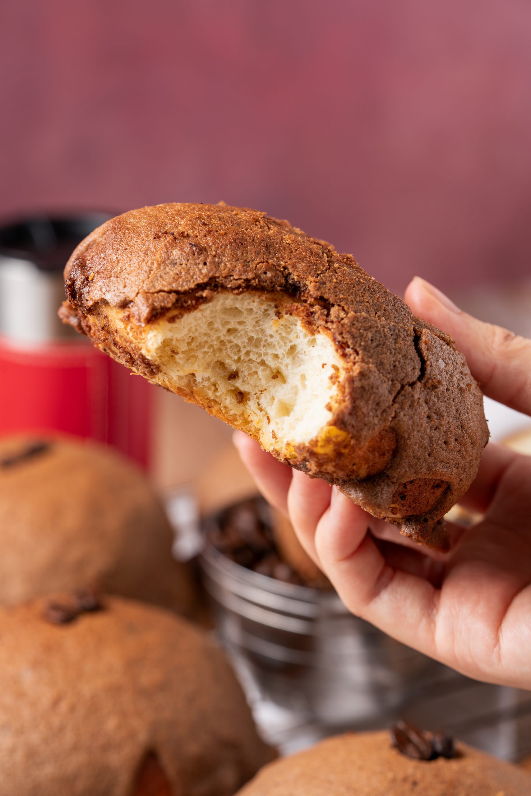 Hand holding a soft and fluffy Pappa Roti bun with a bite taken out, highlighting its airy texture.