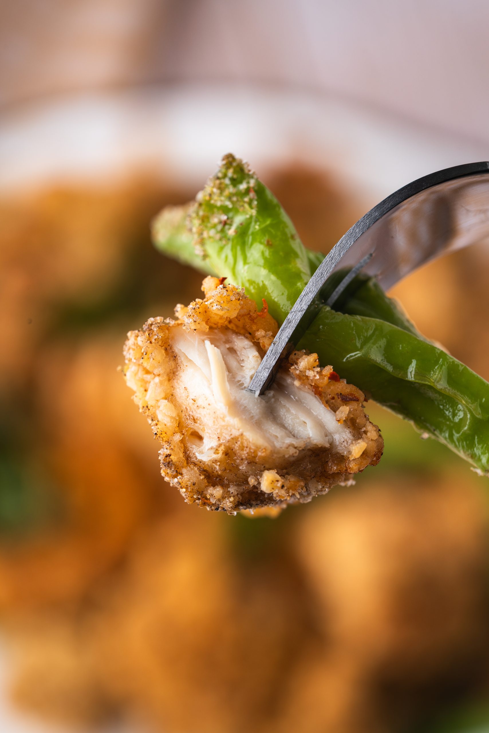 A fork holding a piece of Taiwanese Popcorn Chicken with a crispy coating and basil leaves, with a bite taken