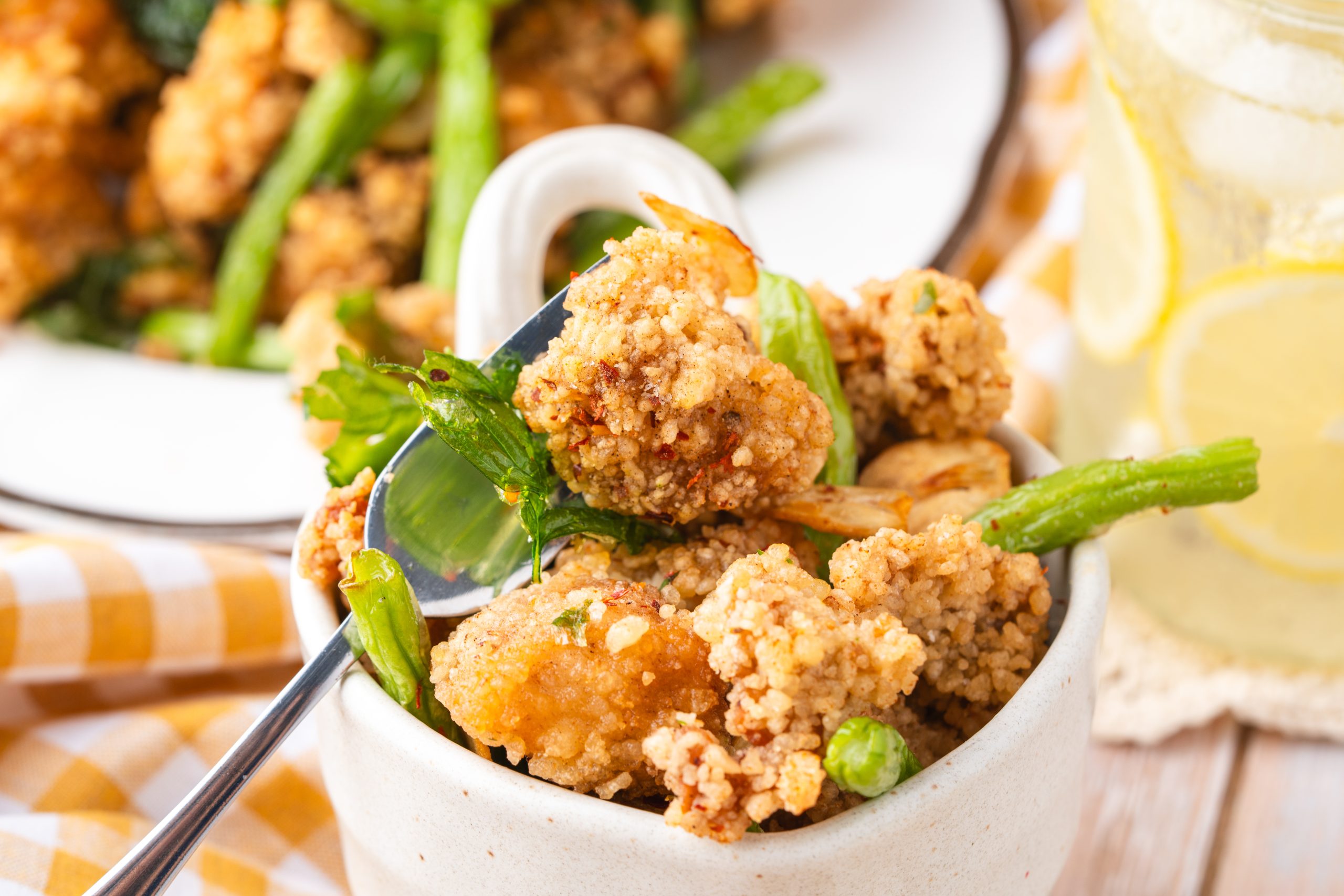 A small bowl filled with golden Taiwanese Popcorn Chicken and green chili peppers, with a glass of lemon drink in the background.