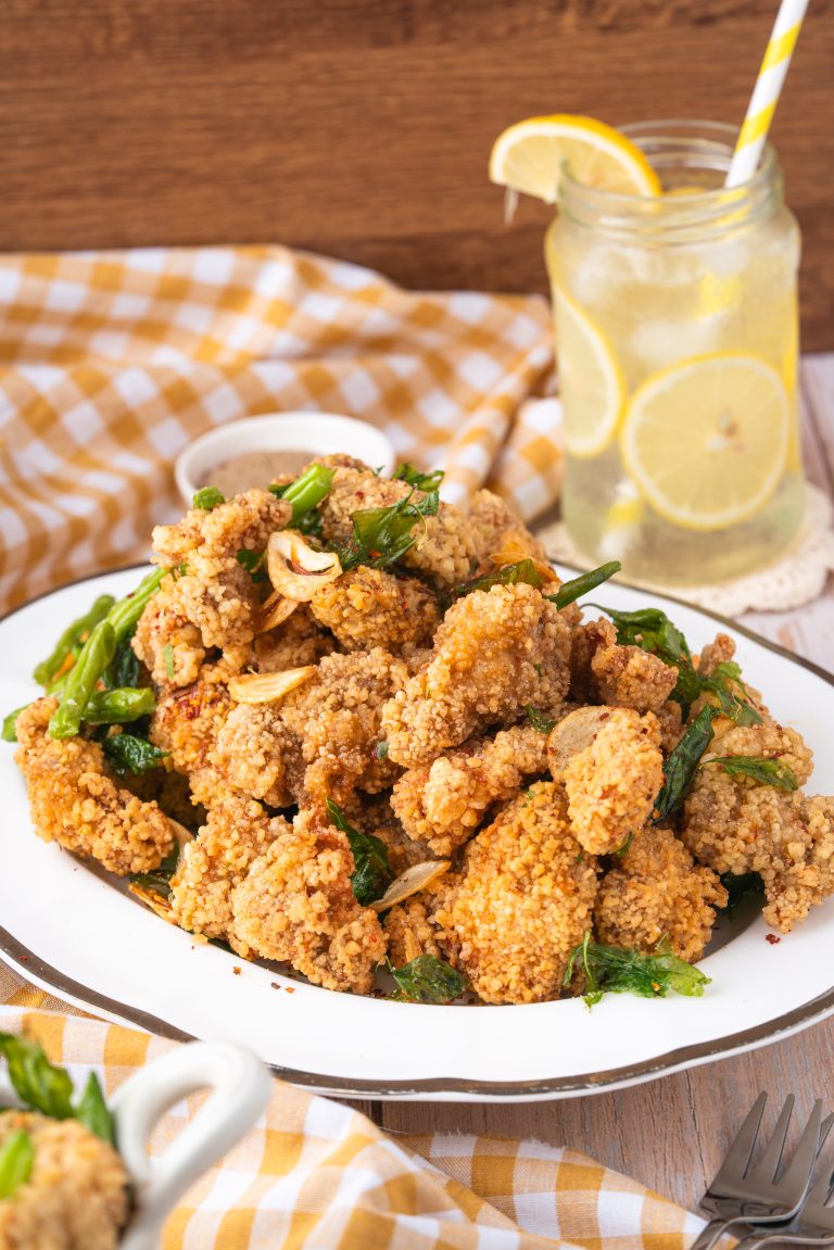 A plate of golden Taiwanese Popcorn Chicken with fried garlic, basil, and green chilies, paired with a refreshing lemon drink on the side.