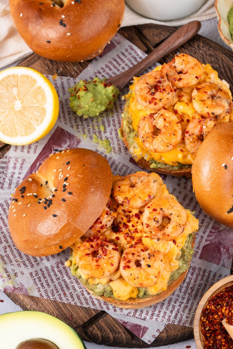 Top view of shrimp avocado bagel sandwich with spicy red pepper flakes and scrambled eggs