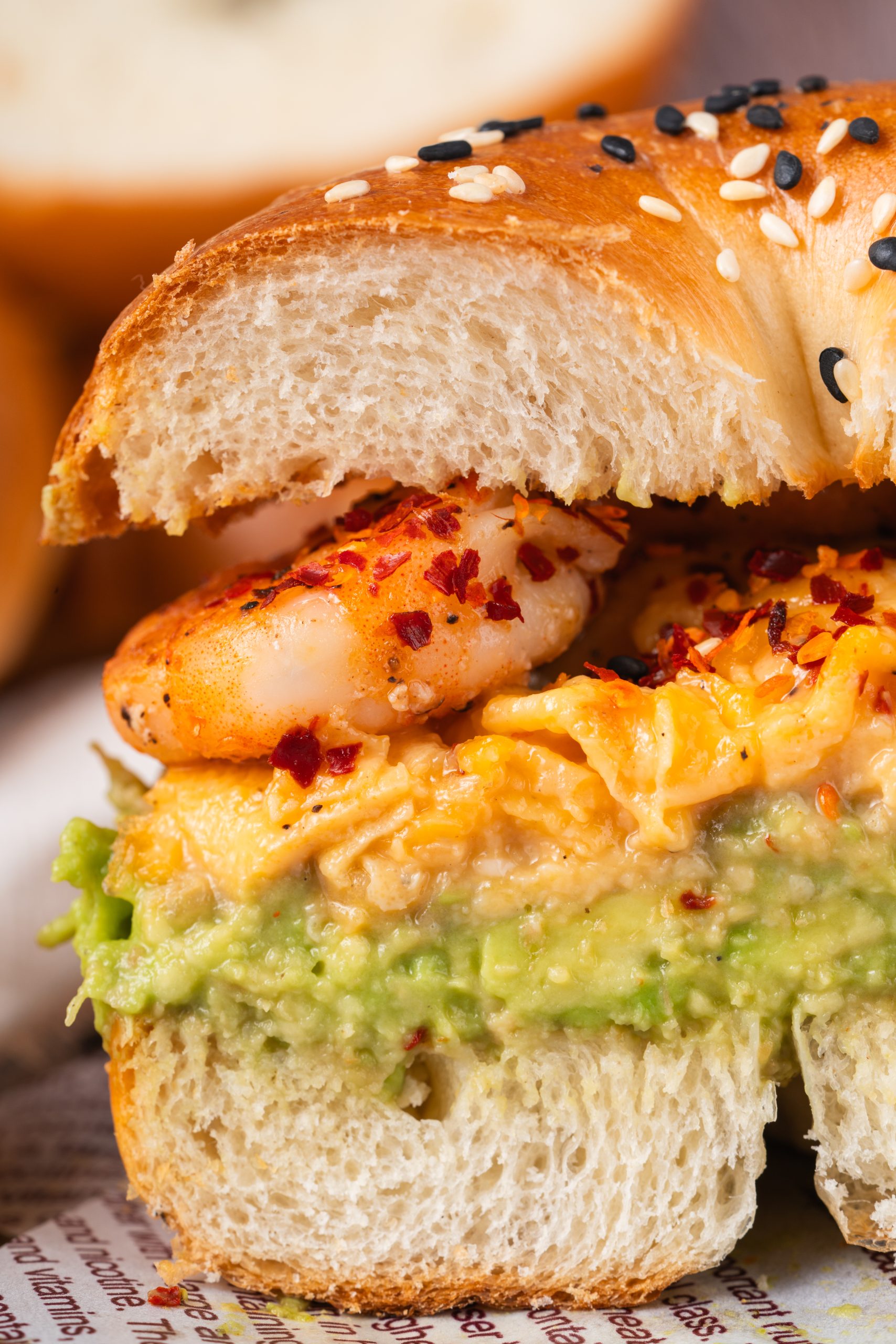 Cross-section of a shrimp avocado bagel sandwich showing the soft interior of the bagel with thick avocado spread, scrambled eggs, and juicy shrimp inside.