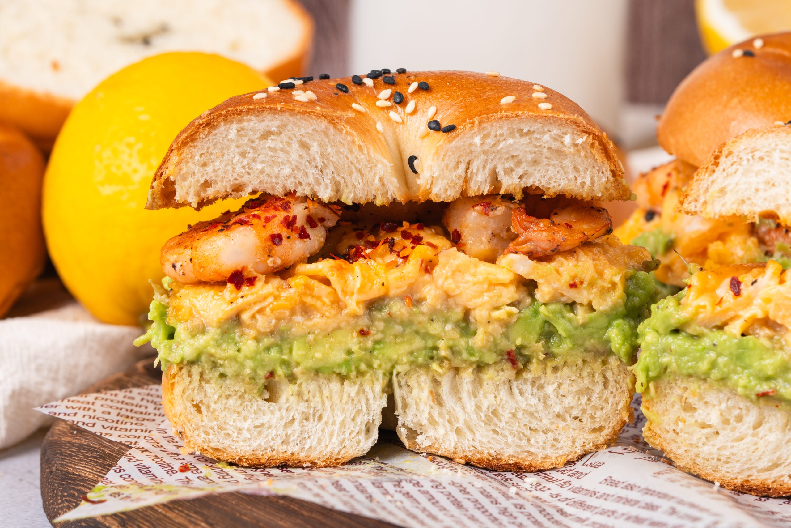 Close-up of halved shrimp avocado bagel sandwich with creamy avocado and fluffy eggs