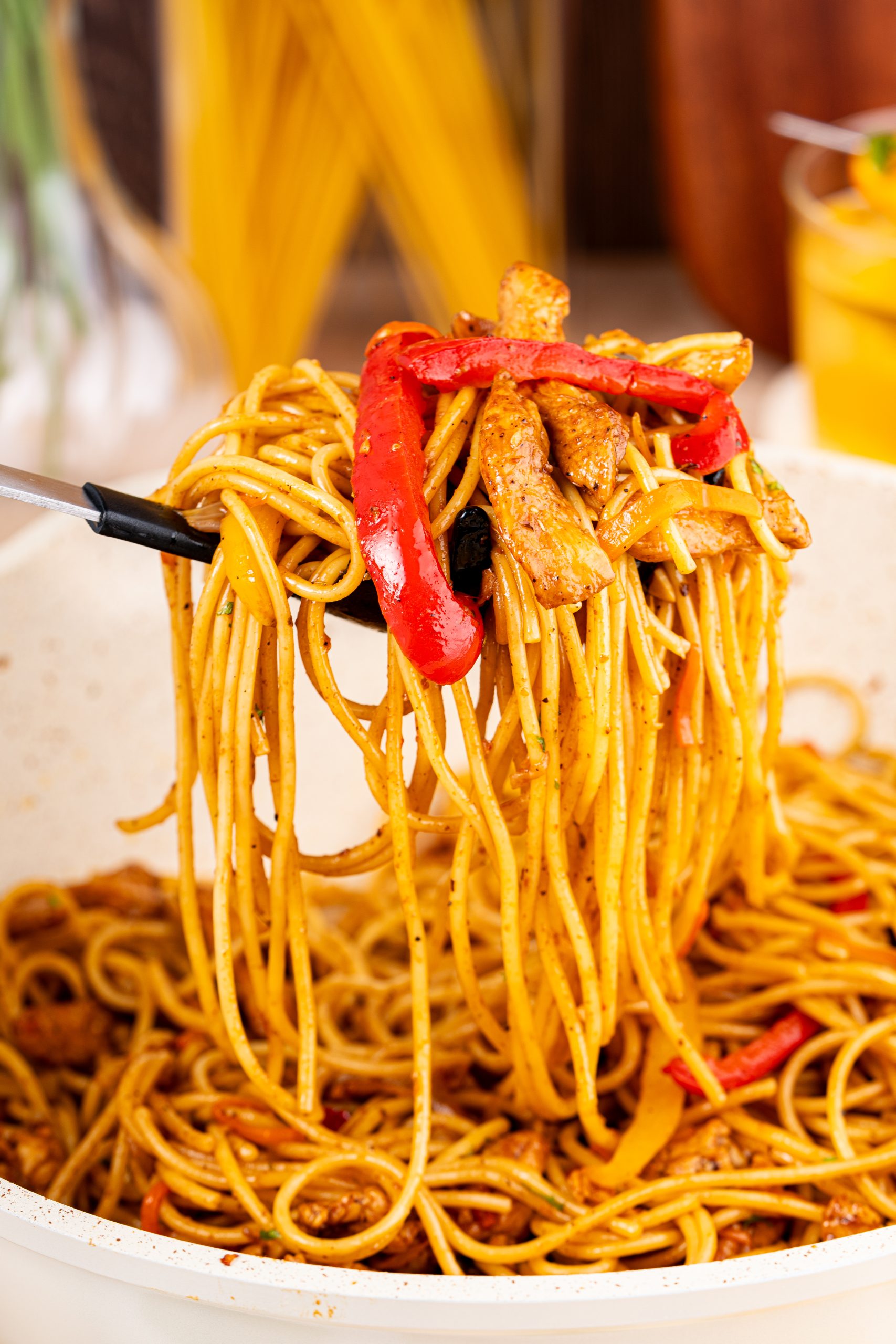 A fork lifting a serving of flavorful Stir-Fry Pasta with red and yellow bell peppers, tossed with tender chicken strips.