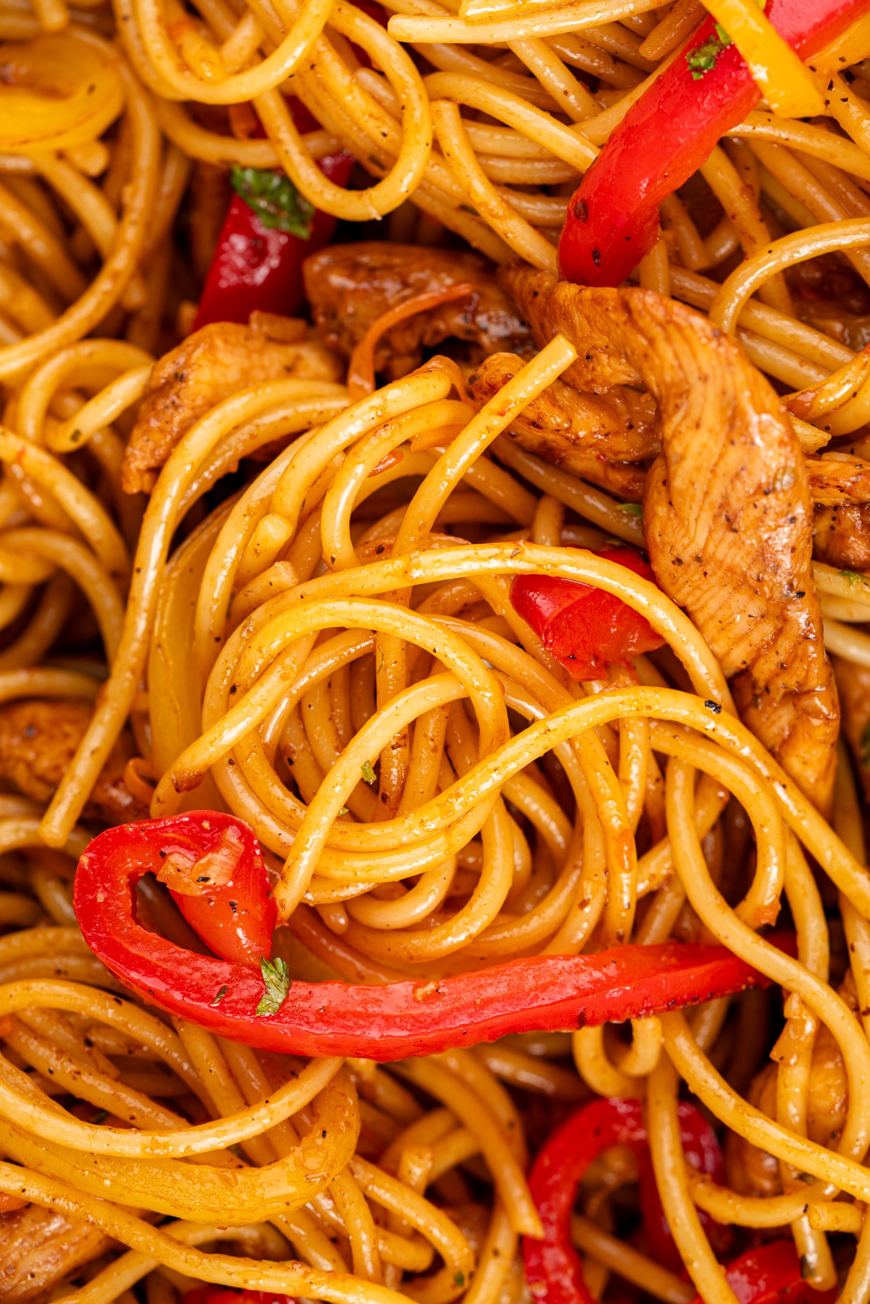 Close-up of Stir-Fry Pasta noodles coated in savory sauce, mixed with colorful bell peppers and juicy chicken slices.