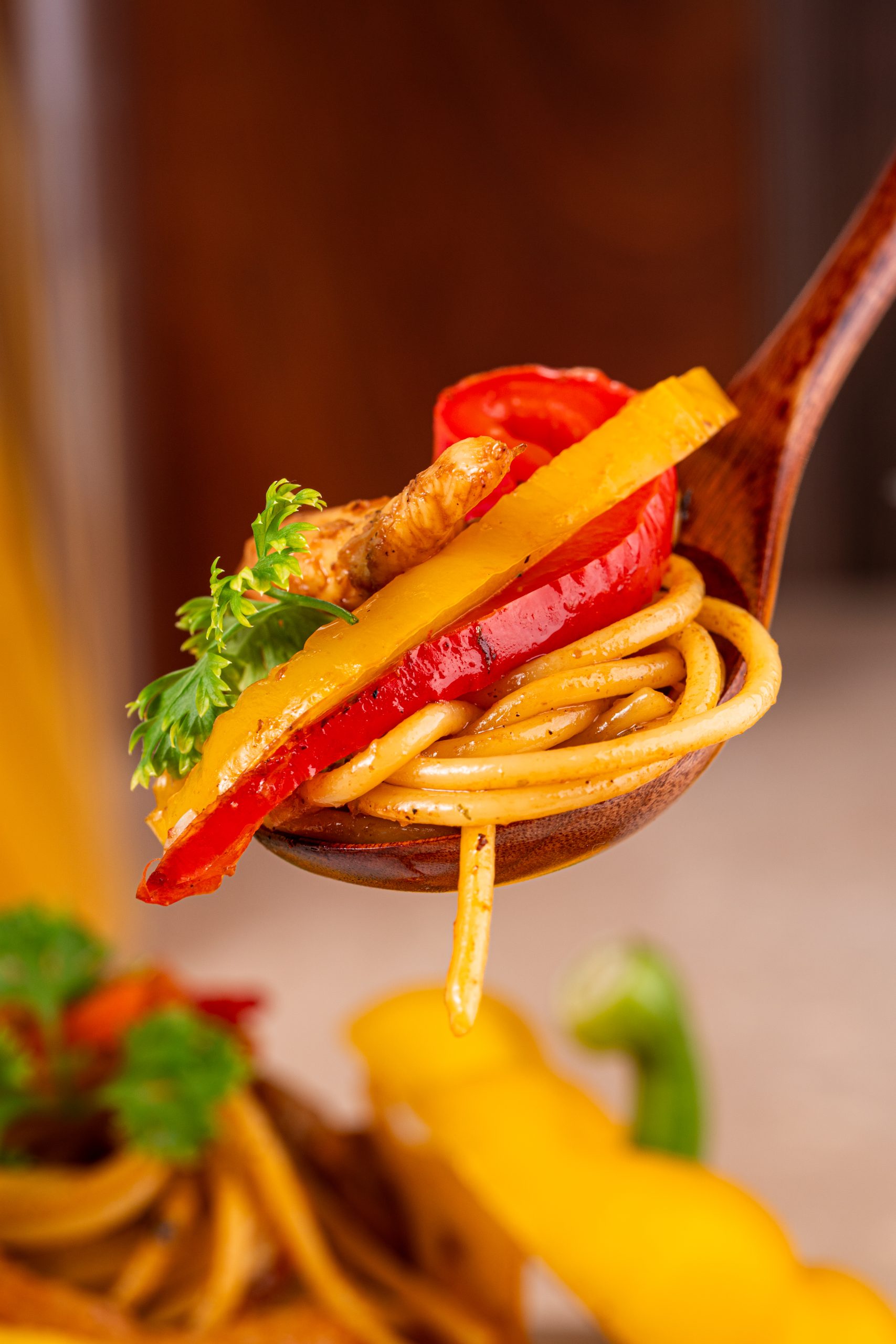 A spoonful of Stir-Fry Pasta with red and yellow bell peppers, chicken, and fresh parsley.