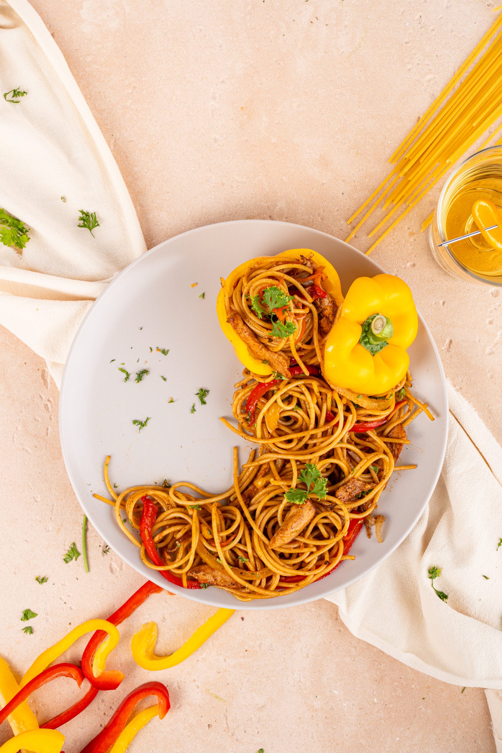 Overhead view of a plate of Stir-Fry Pasta with bell peppers and herbs on a light background, styled with raw pasta for decoration.