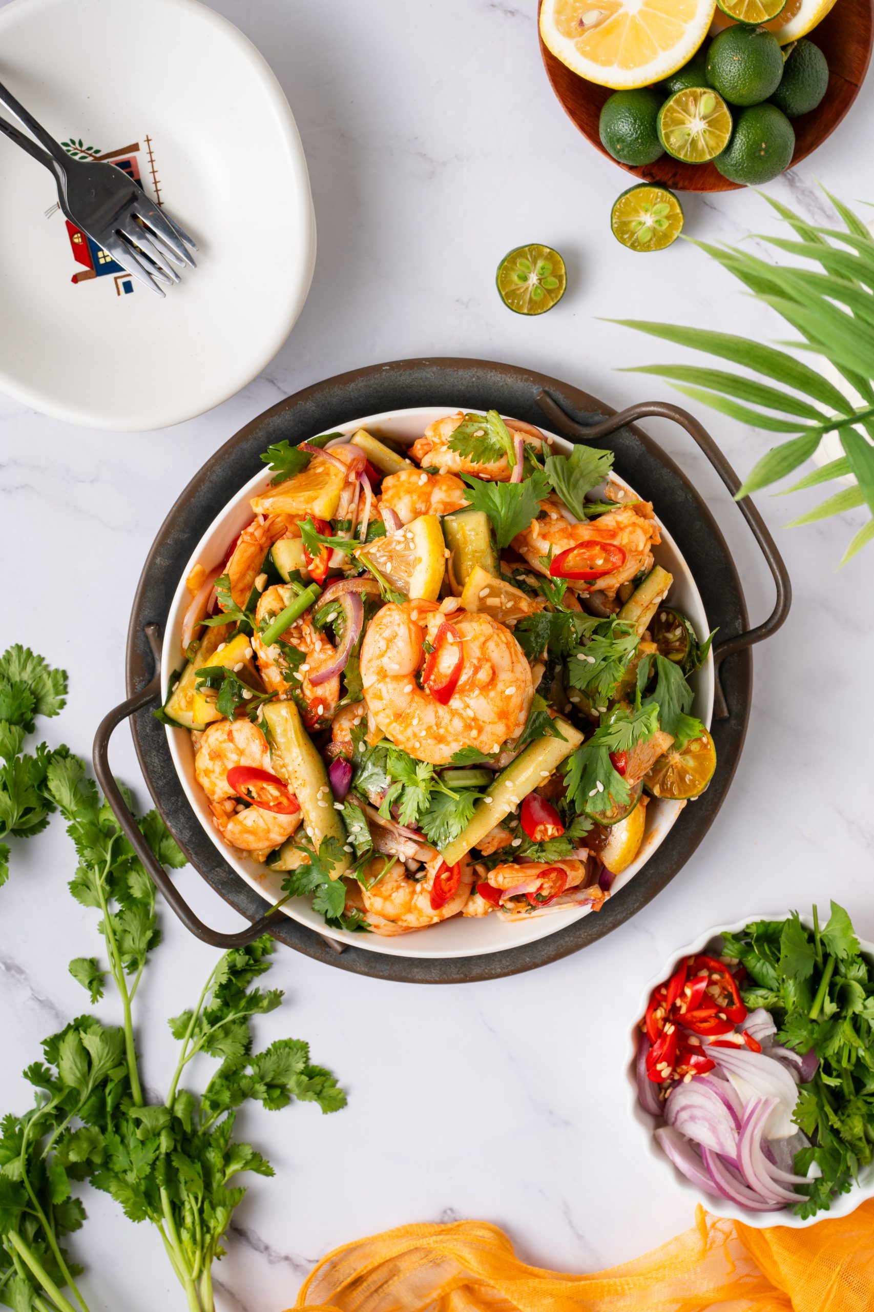 Overhead view of vibrant Sweet and Sour Shrimp Salad with fresh shrimp, cucumber, red chili, onion, and cilantro, garnished with lime and sesame seeds on a marble table.