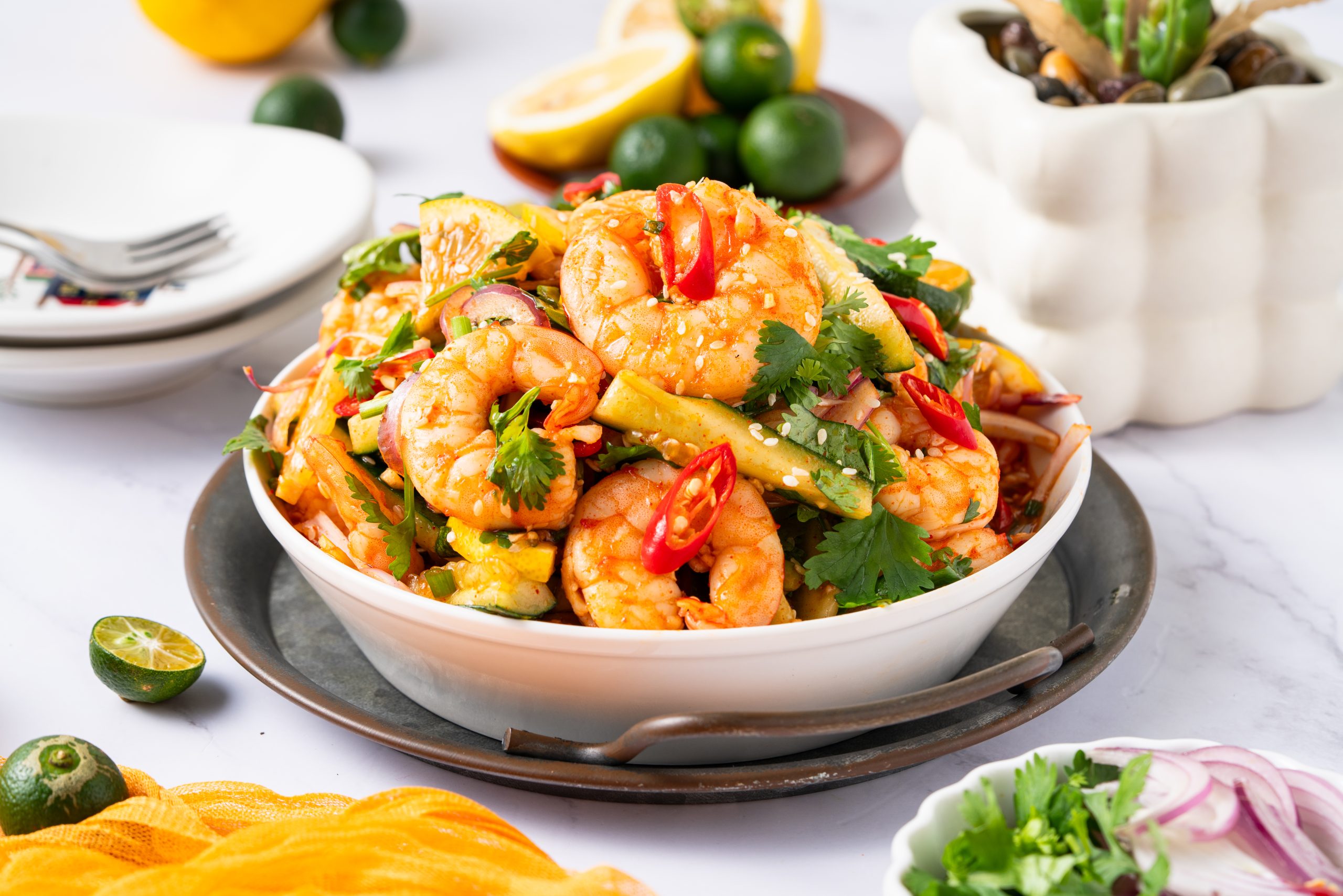 Side view of Sweet and Sour Shrimp Salad served in a white bowl, garnished with cilantro, chili, and lime.
