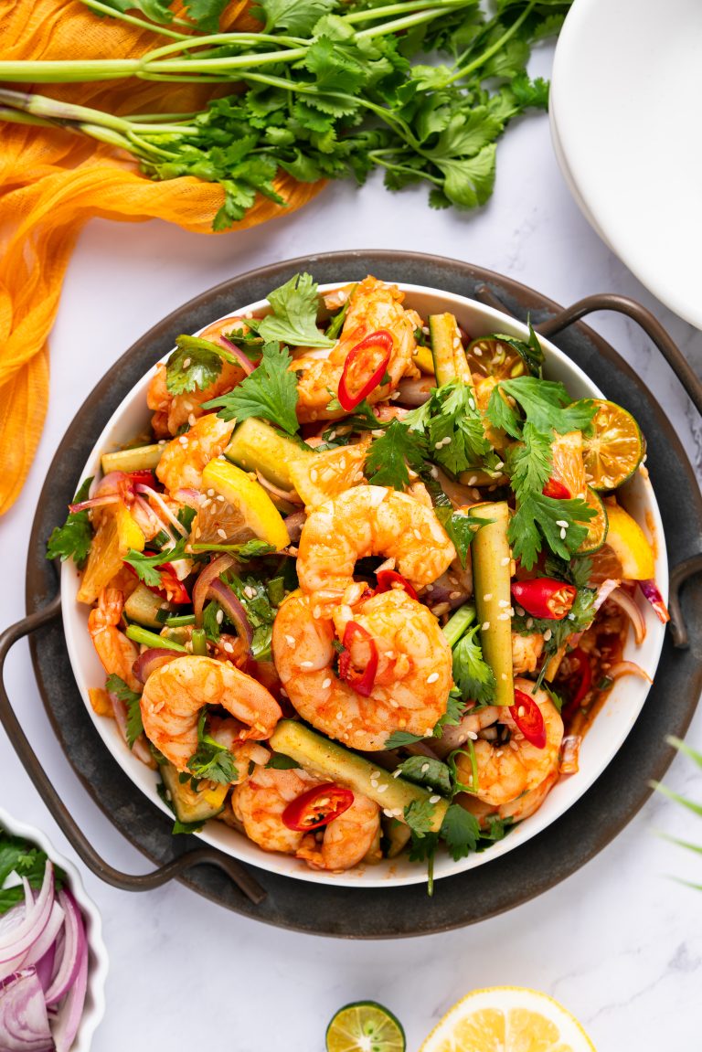 Overhead view of a vibrant Sweet and Sour Shrimp Salad with lemon, cucumber, cilantro, and chili in a white bowl.