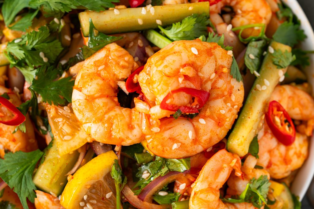 Close-up of colorful Sweet and Sour Shrimp Salad with fresh shrimp, cucumber, red chili, and sesame seeds.