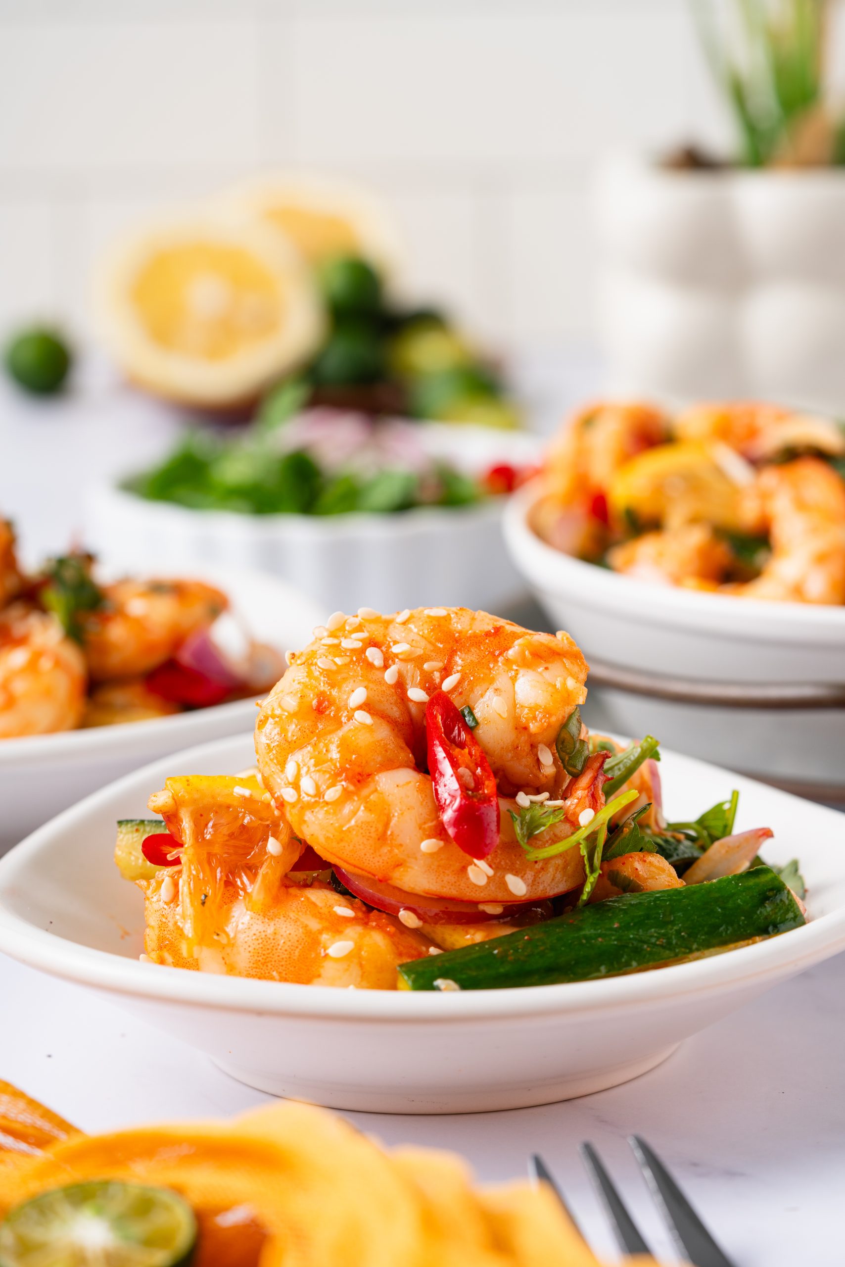 Bowl of Sweet and Sour Shrimp Salad topped with sesame seeds, chili slices, and herbs, surrounded by fresh ingredients.