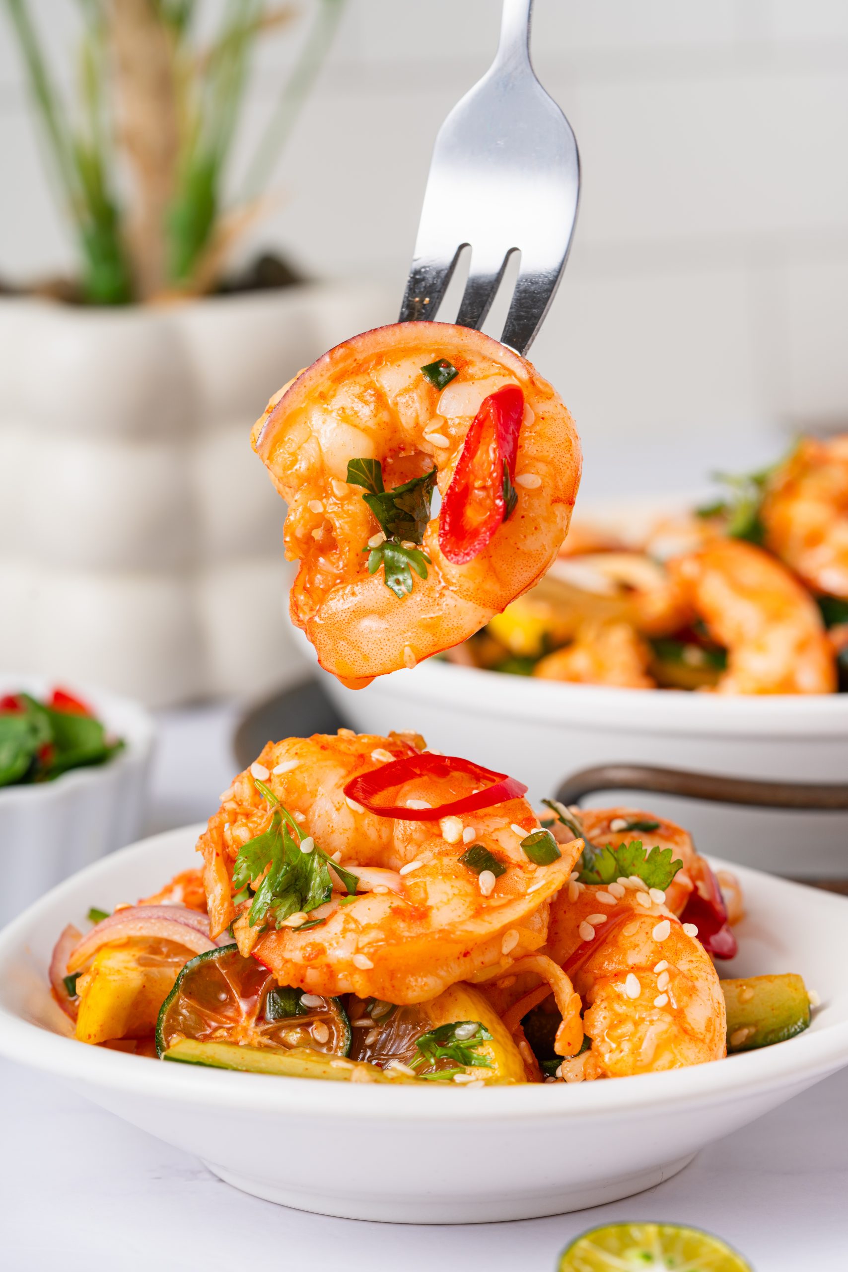 Fork holding a shrimp coated in zesty Sweet and Sour Shrimp Salad dressing with herbs and sesame seeds.