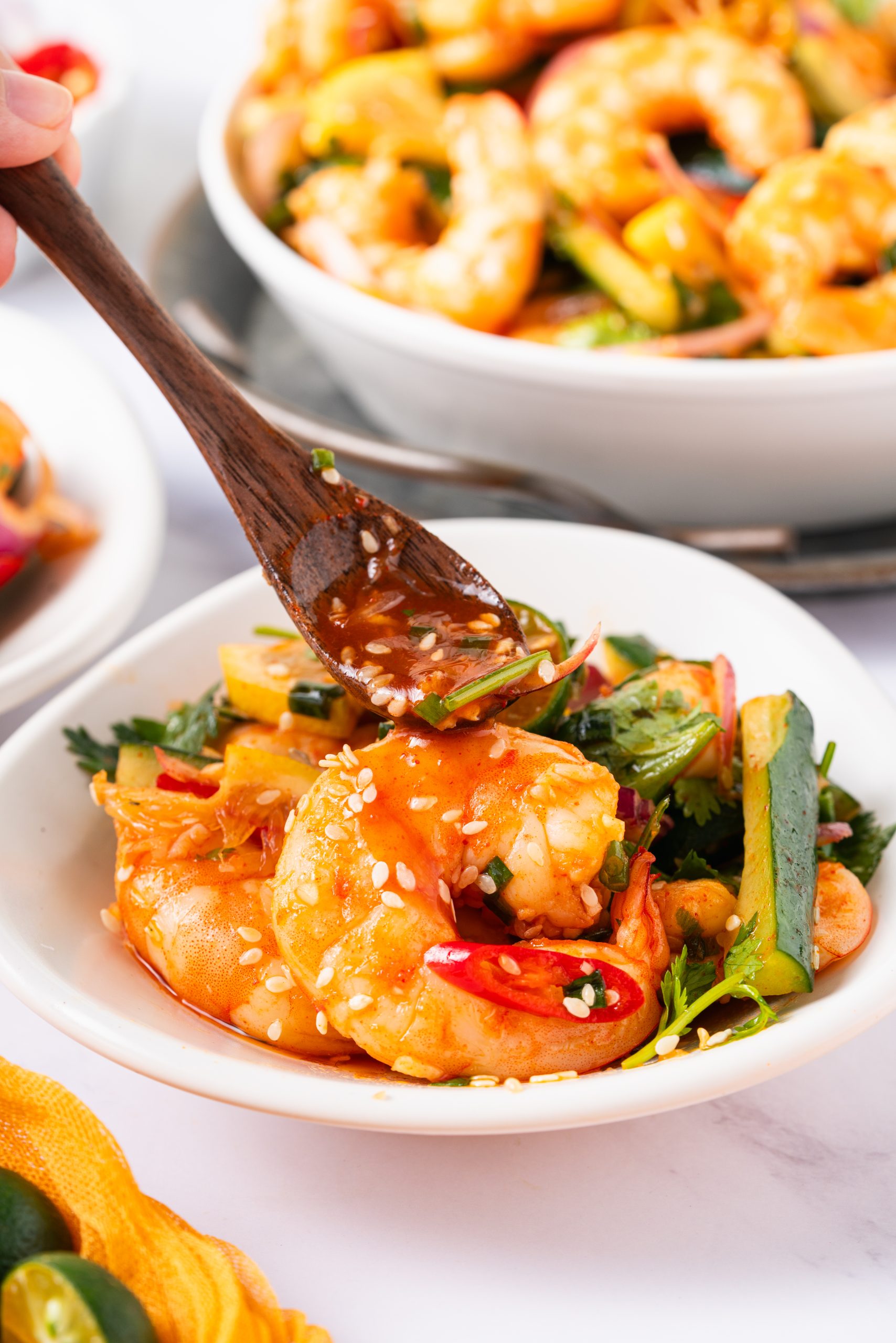 A wooden spoon drizzling tangy dressing over a serving of Sweet and Sour Shrimp Salad with shrimp and vegetables.