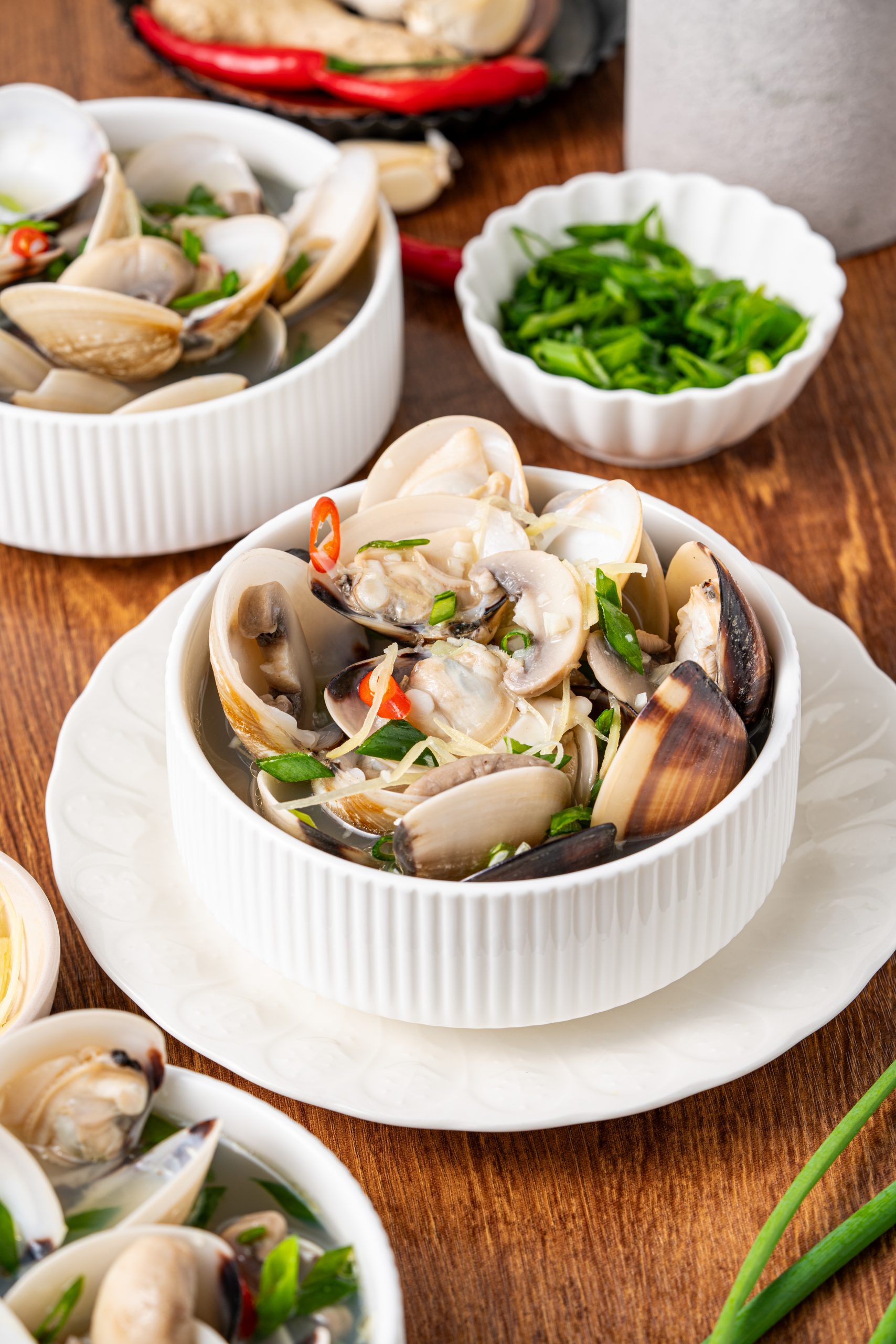 “Close-up of a bowl of clam soup filled with clams, mushrooms, ginger, and chili slices.”