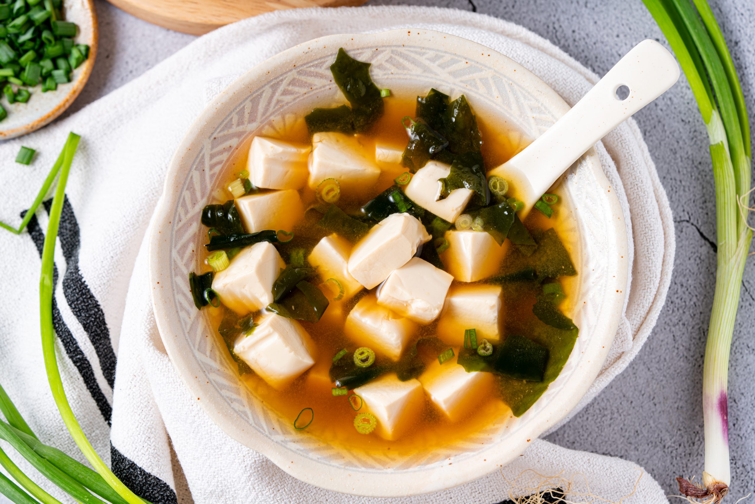 Overhead shot of Japanese miso soup served with tofu cubes, seaweed, and green onions, surrounded by fresh scallions.