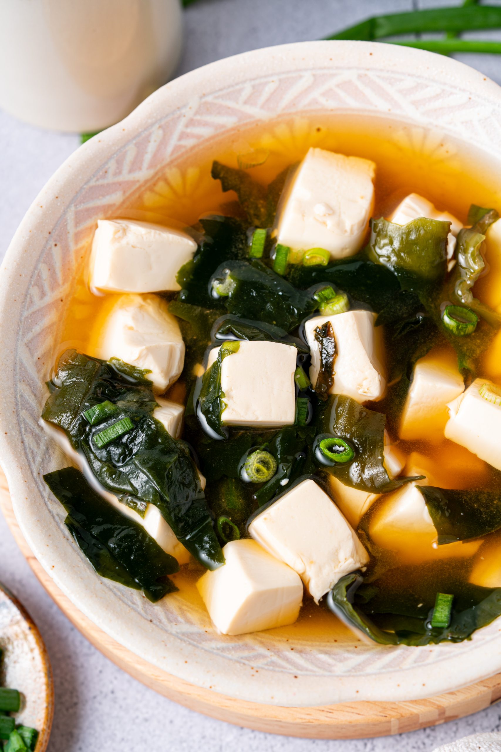 Close-up of a bowl of traditional Japanese miso soup with soft tofu, wakame seaweed, and chopped green onions in light broth.