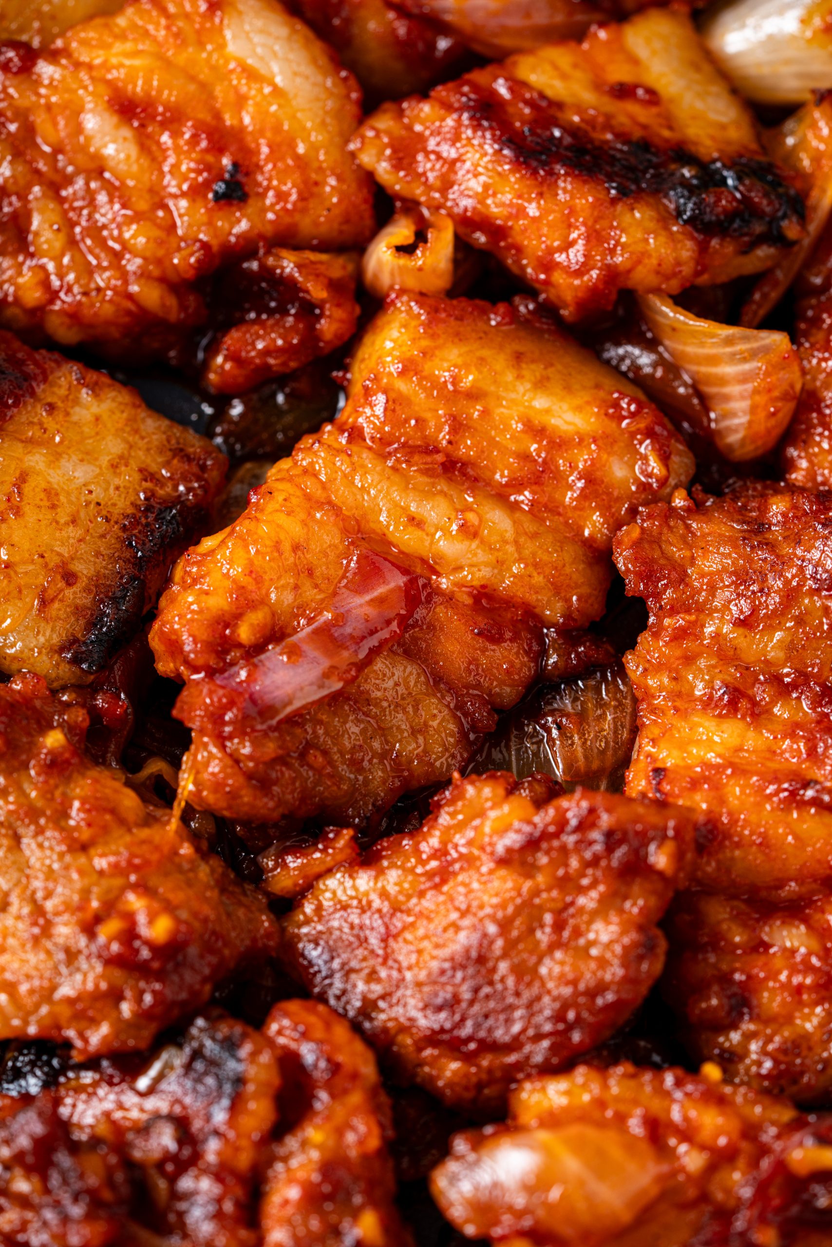 Extreme close-up of caramelized pieces of Korean stir-fried pork coated in gochujang sauce with onions.