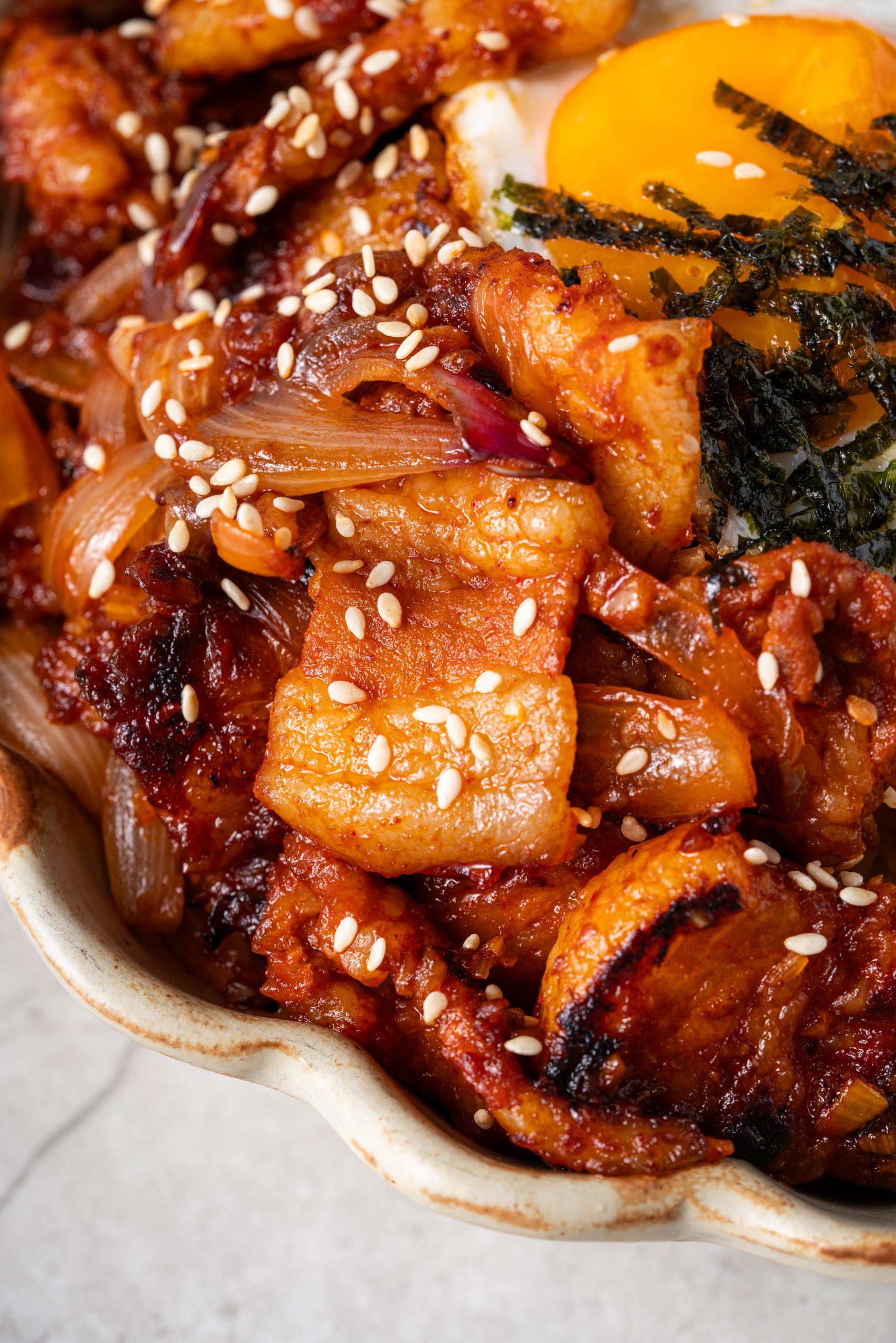 Close-up of Korean stir-fried pork with onions and sesame seeds coated in a rich red chili sauce.