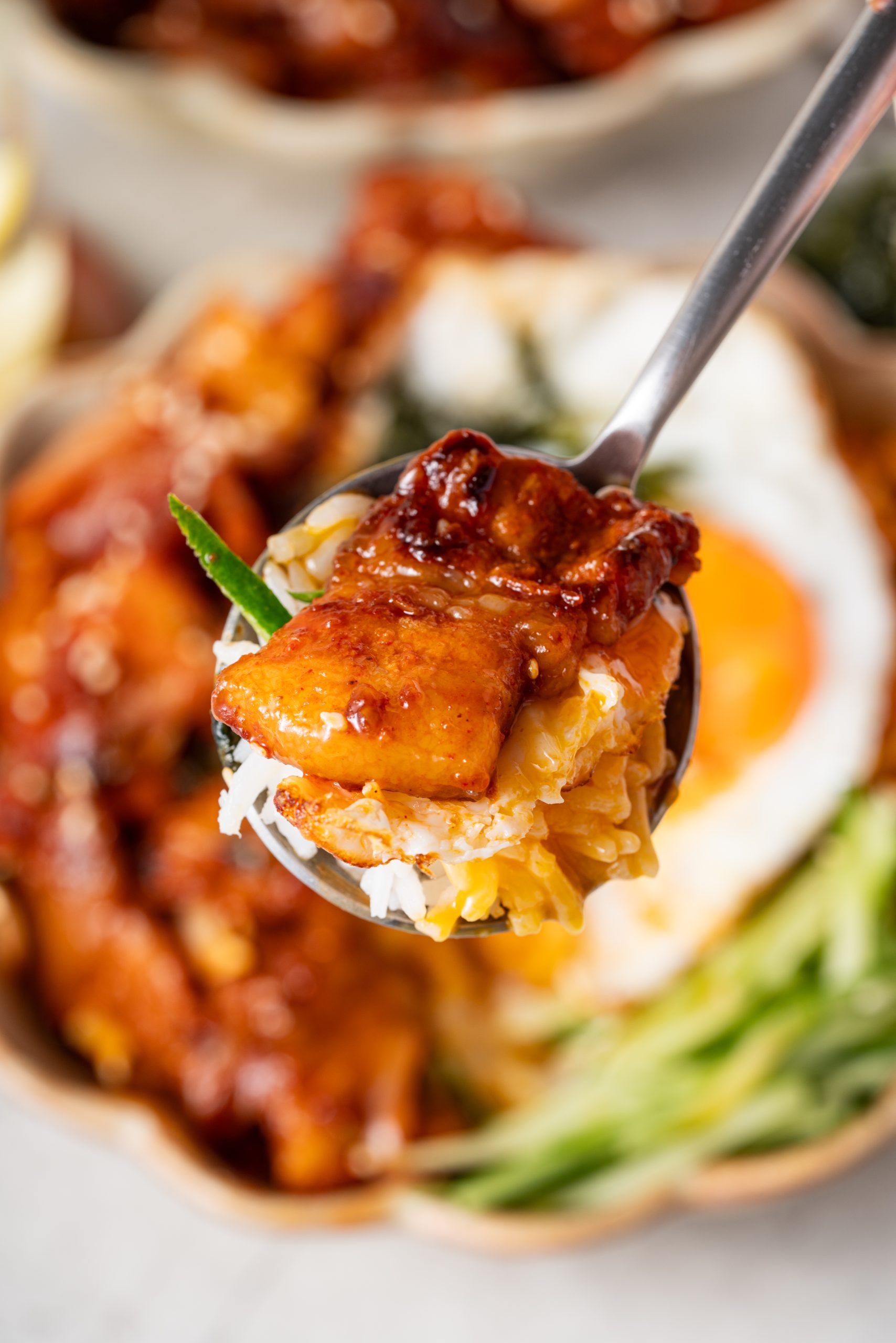 A spoonful of Korean pork stir fry served over rice with a piece of fried egg, glistening with spicy sauce.