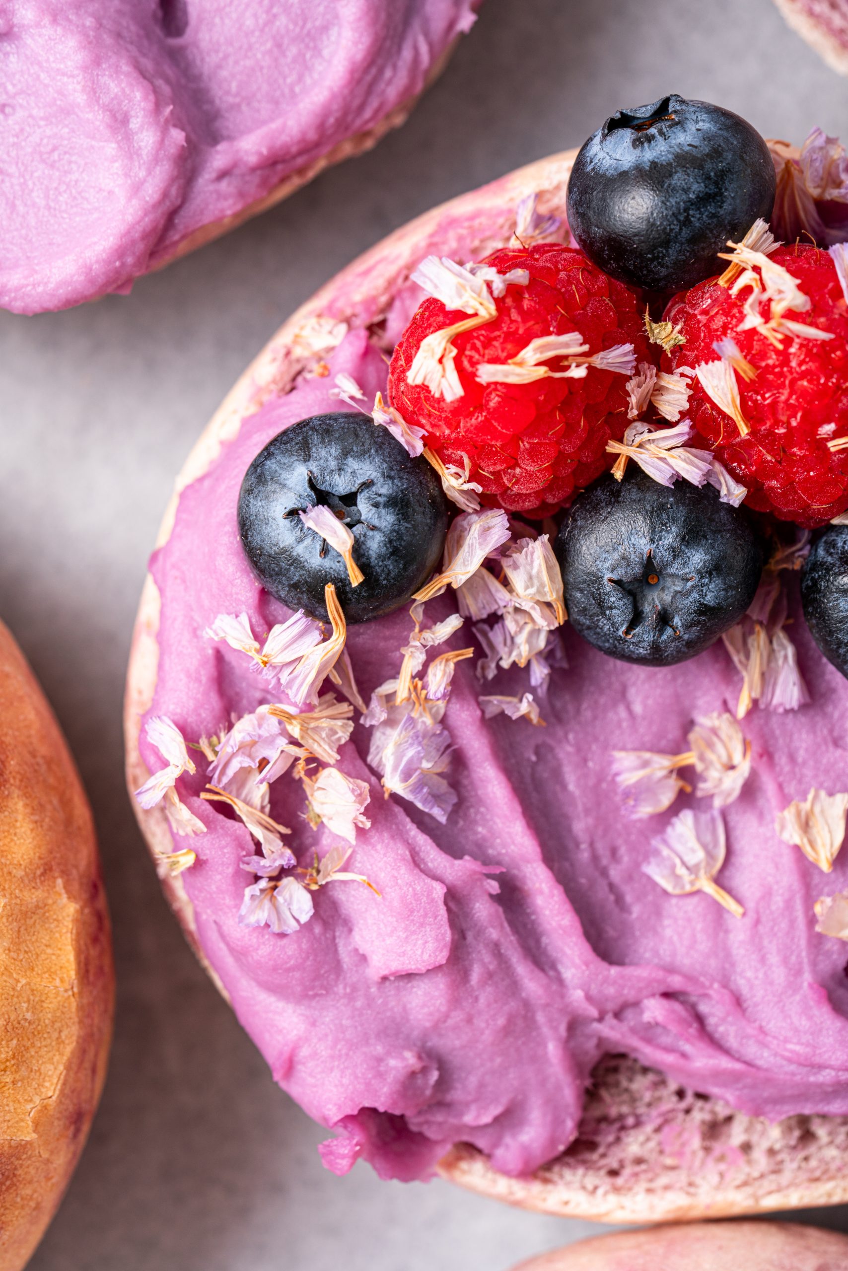 Macro shot of a Purple Sweet Potato Bagel half topped with purple sweet potato spread, blueberries, and raspberries.