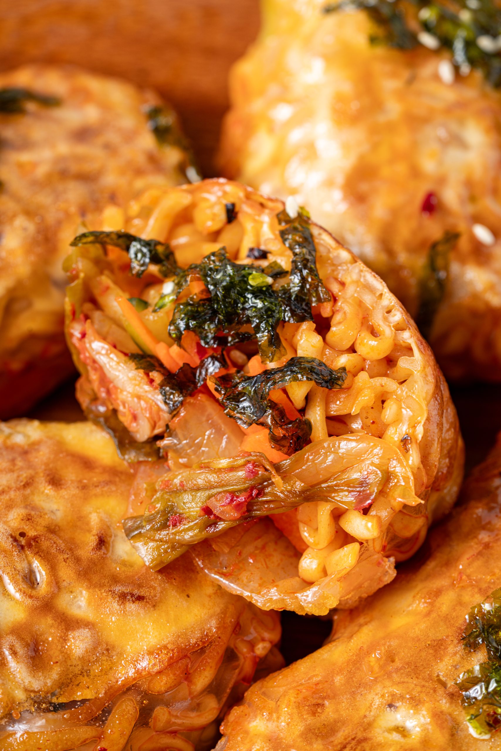 A close-up of a cut ramen spring roll showing tightly packed noodles, julienned vegetables, kimchi, and seaweed flakes inside the crispy wrapper.
