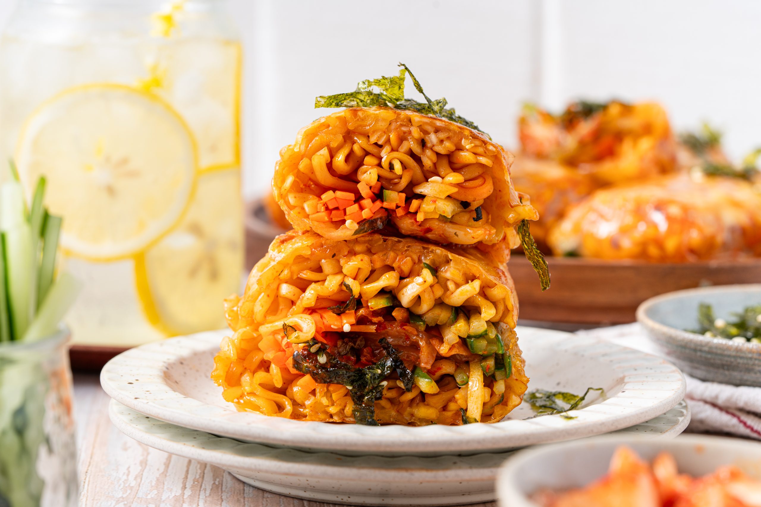 Two halves of a stacked ramen spring roll on a white plate, showcasing the vibrant orange noodles and mixed vegetables inside.