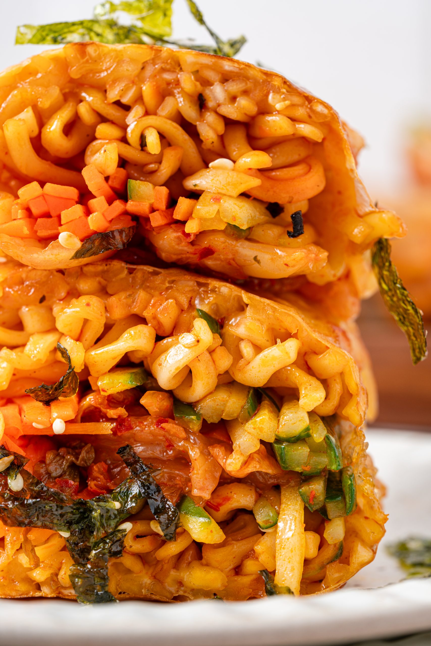“Close-up of a sliced ramen spring roll showing tightly packed noodles, diced vegetables, kimchi, and seaweed inside a crispy wrapper.”